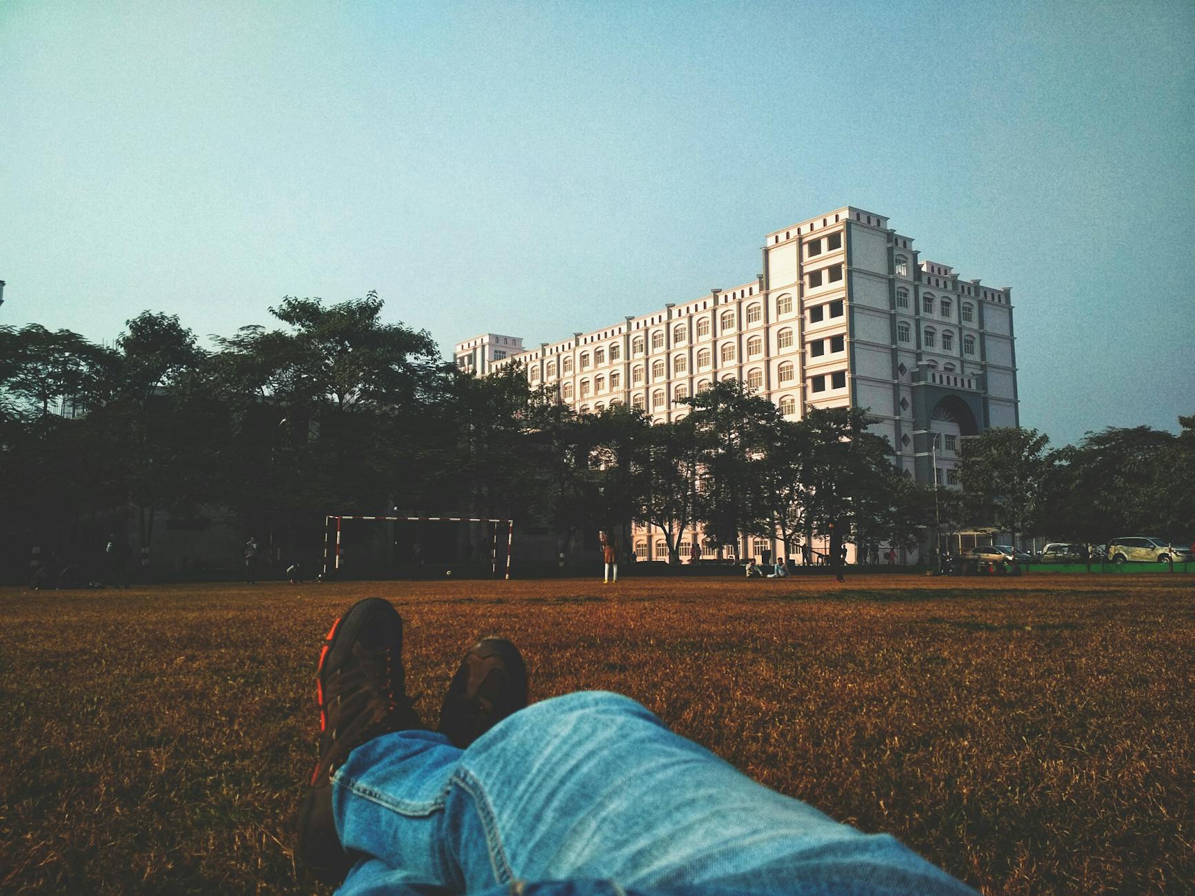 Person relaxing outdoors viewing a university building with blue sky and green surroundings.
