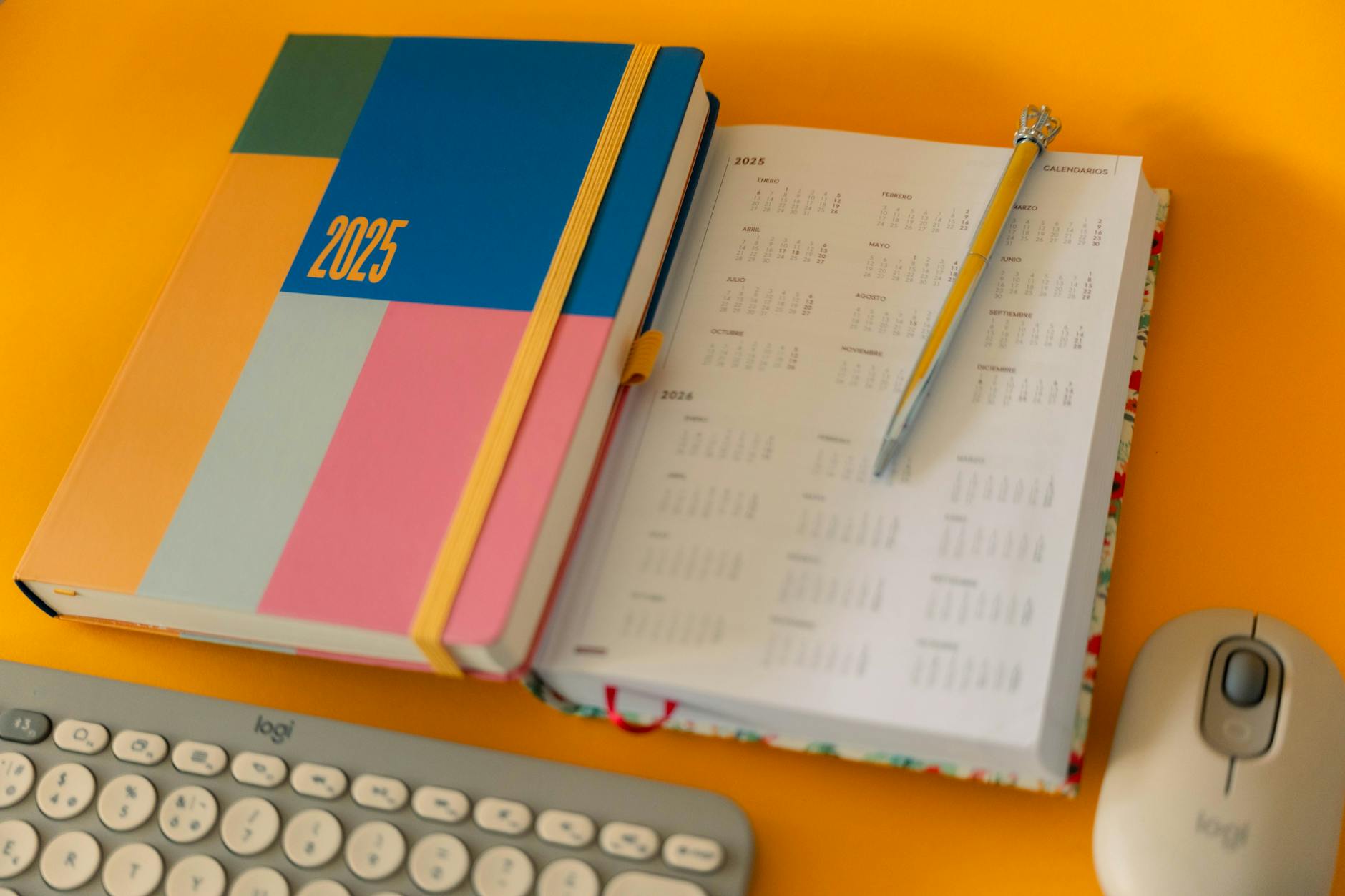Colorful 2025 planner and calendar with pen on a bright yellow desk.