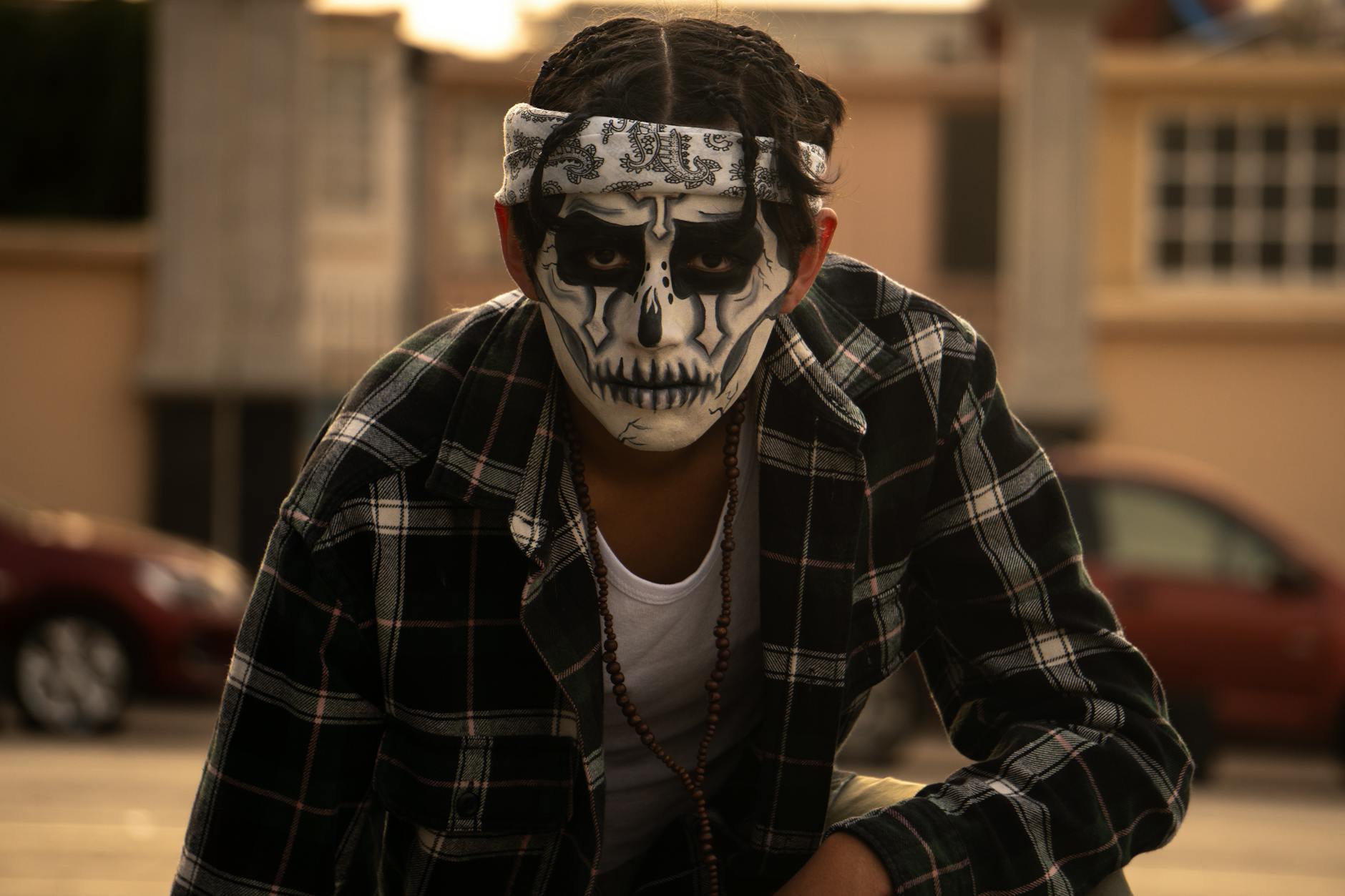 Young man with skull face paint and plaid shirt celebrating Day of the Dead outdoors.