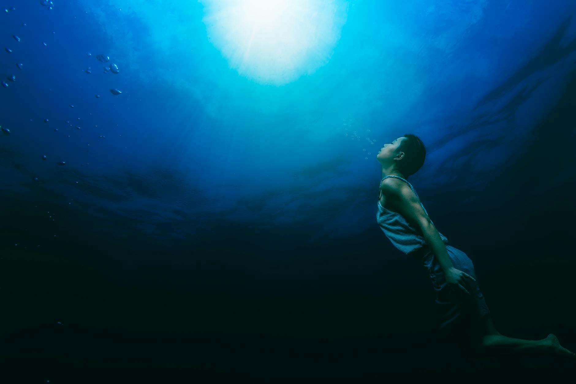 A serene scene of a person swimming underwater towards sunlight, capturing tranquility and exploration.
