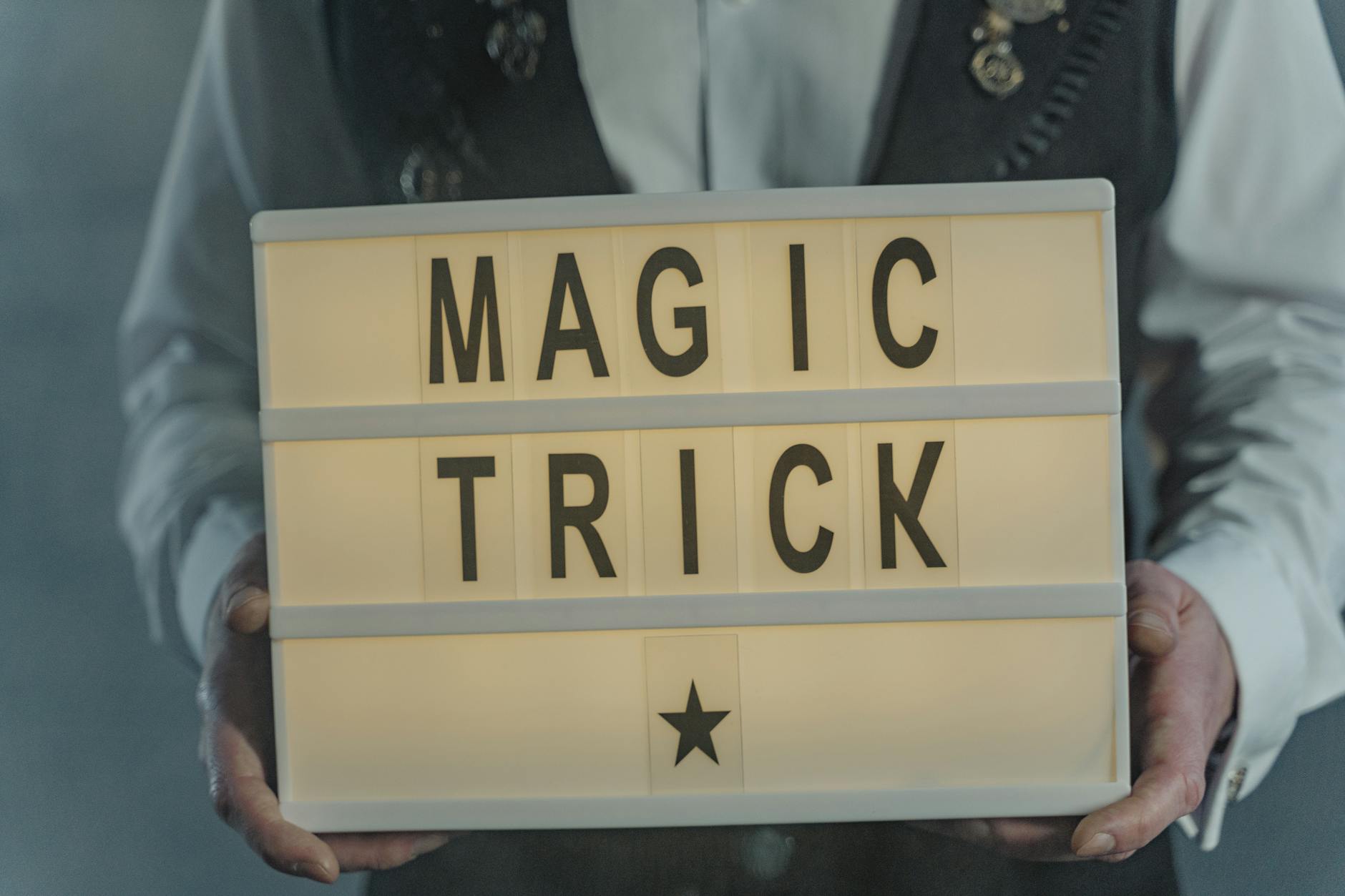 A magician in a vest holds a lightbox displaying 'Magic Trick', creating a mysterious and intriguing atmosphere.