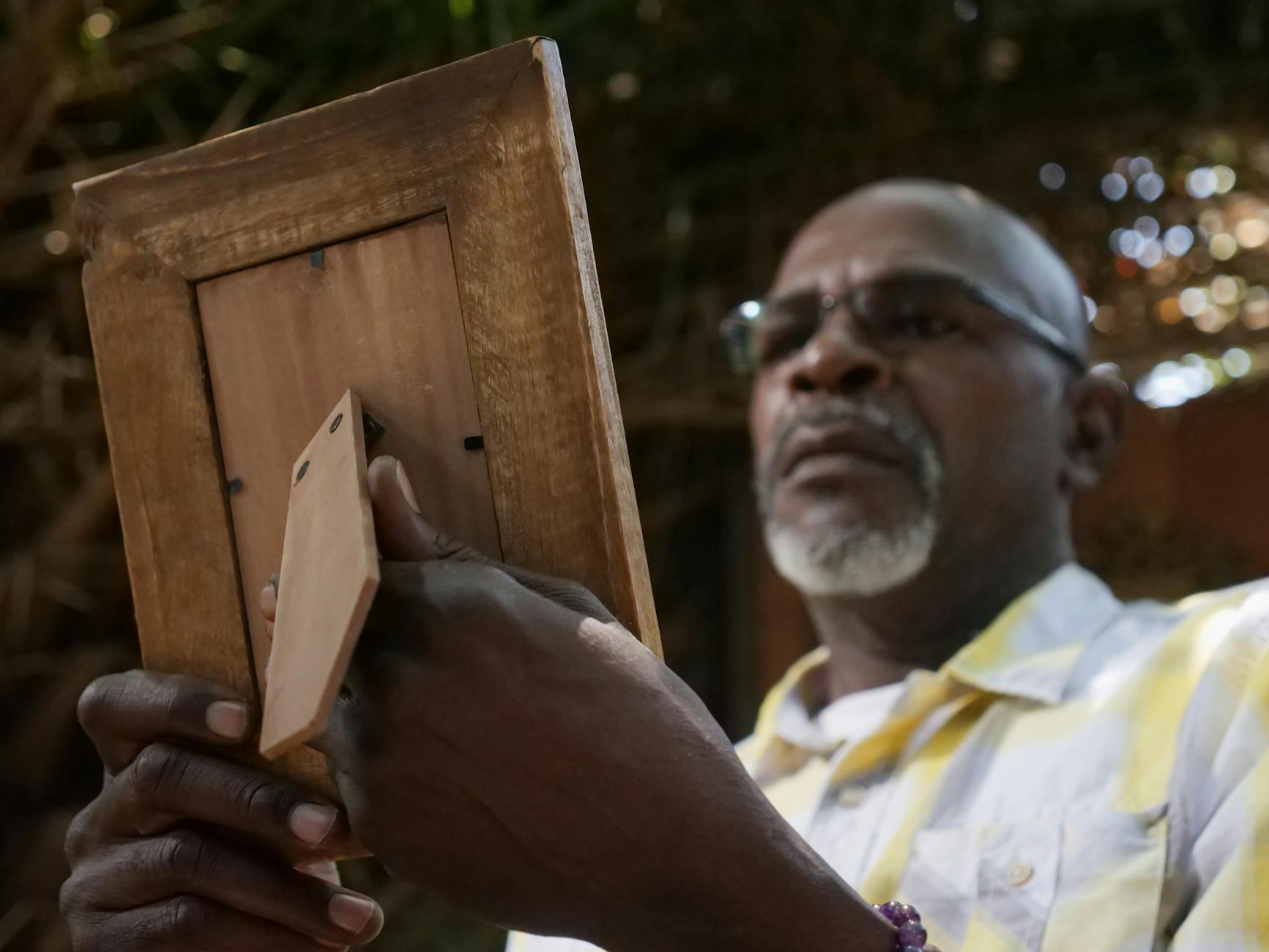 A thoughtful elderly man examines an empty wooden picture frame, evoking nostalgia.