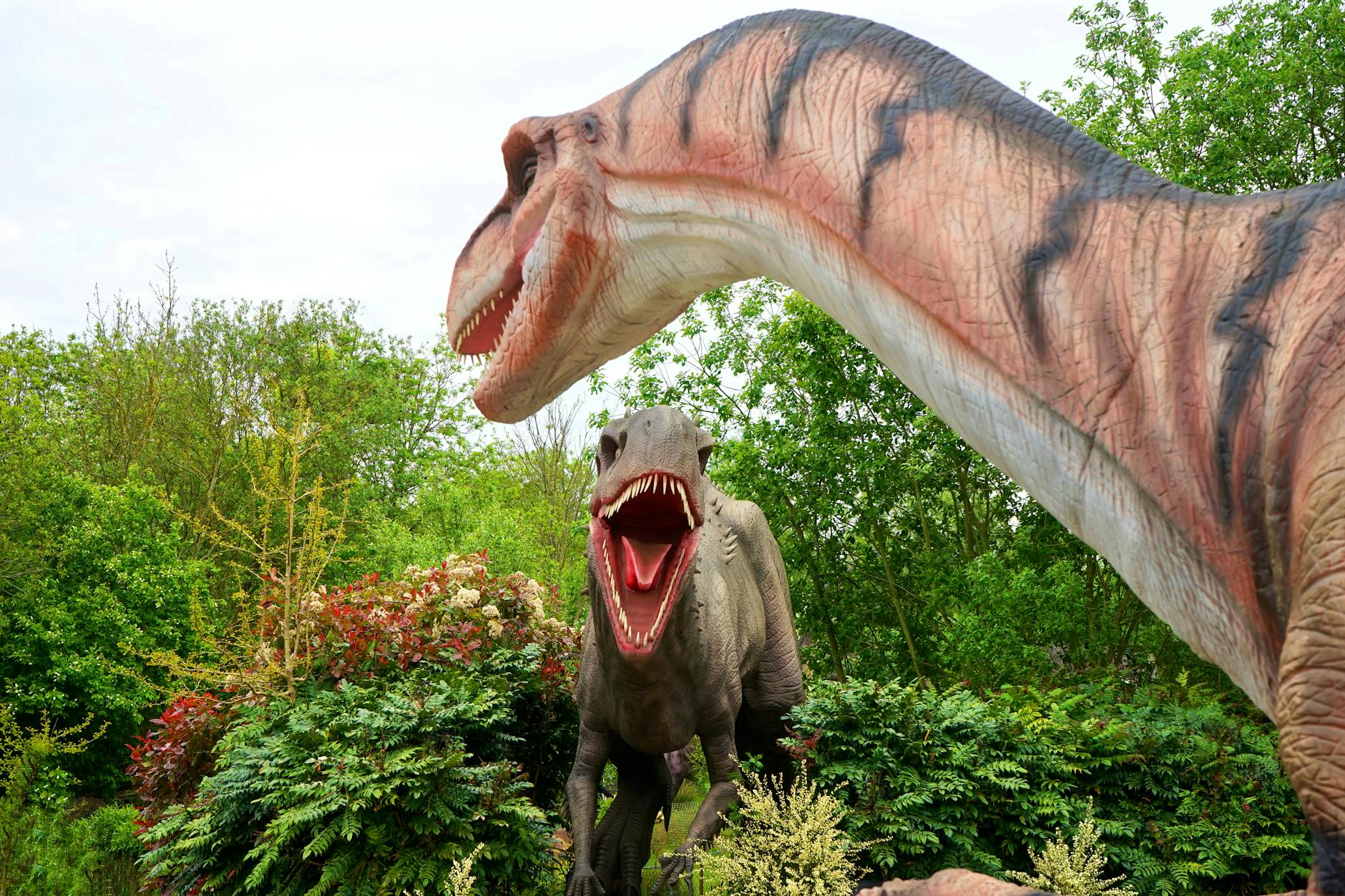 Realistic dinosaur sculptures in a lush park setting, evoking prehistoric times.