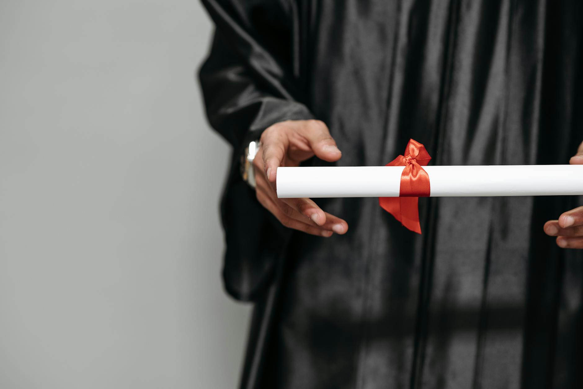 Close-up of a graduate holding a diploma tied with a red ribbon, symbolizing achievement.