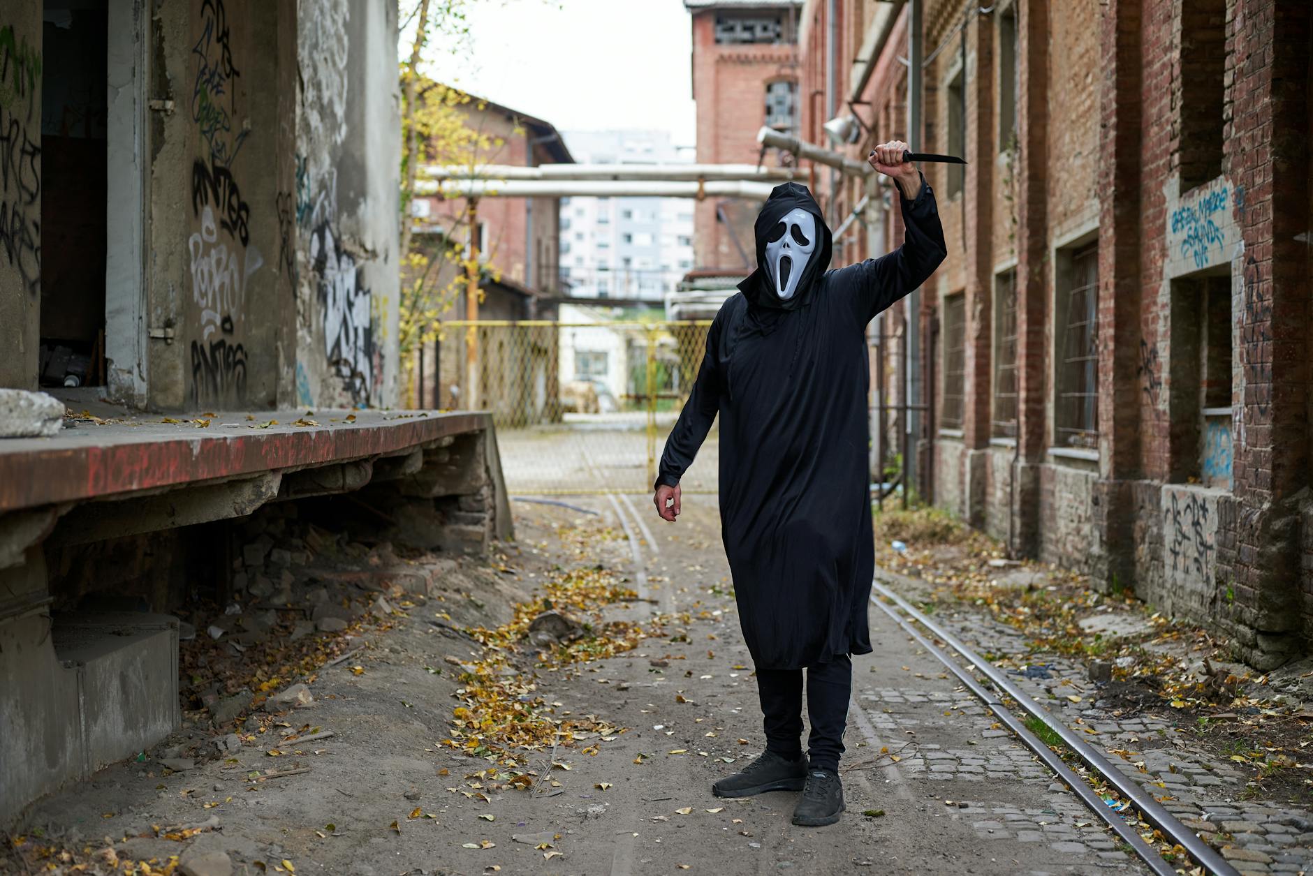Person in ghost mask and robe posing in a graffitied alleyway in Belgrade.