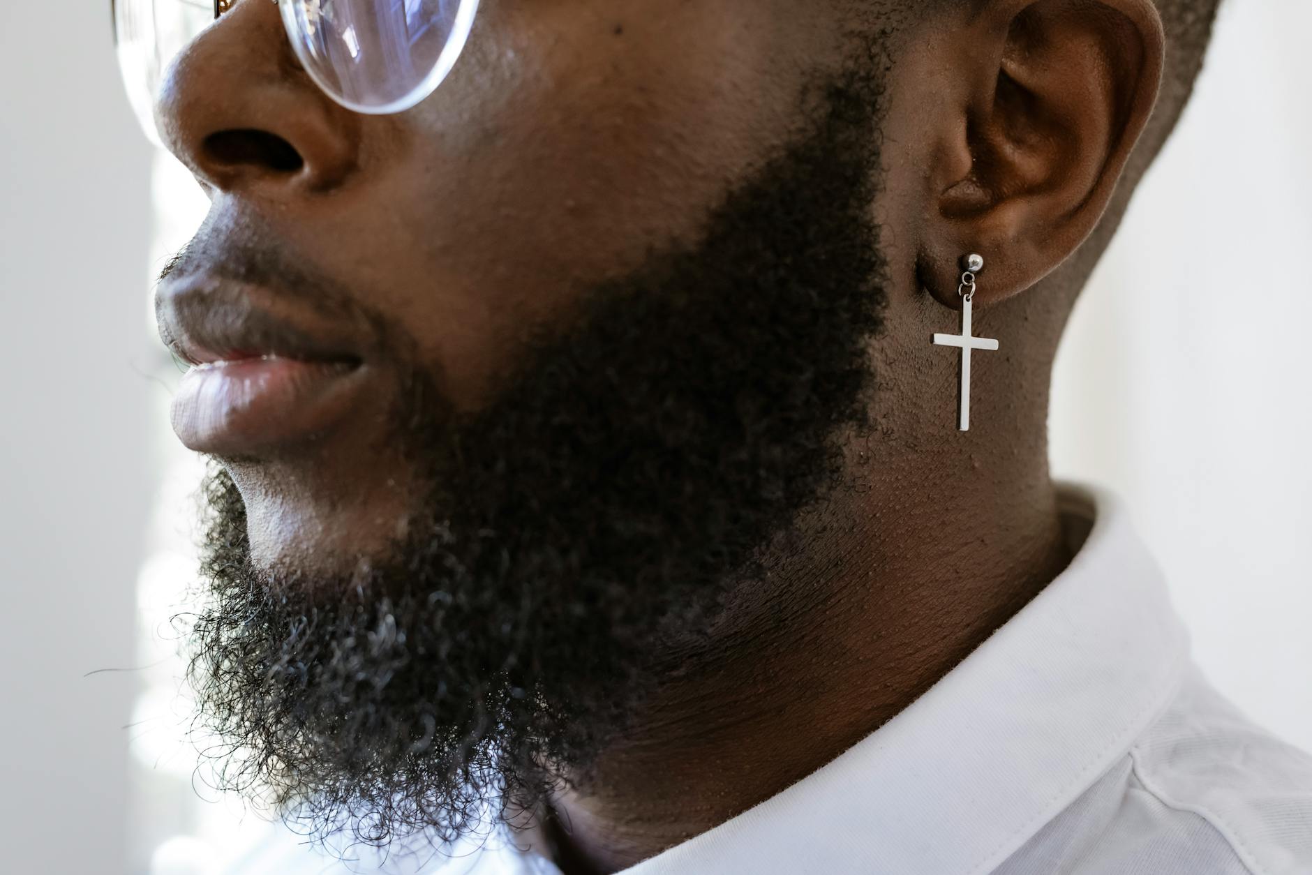 Close-up of a man wearing a cross earring and glasses, showcasing modern style.