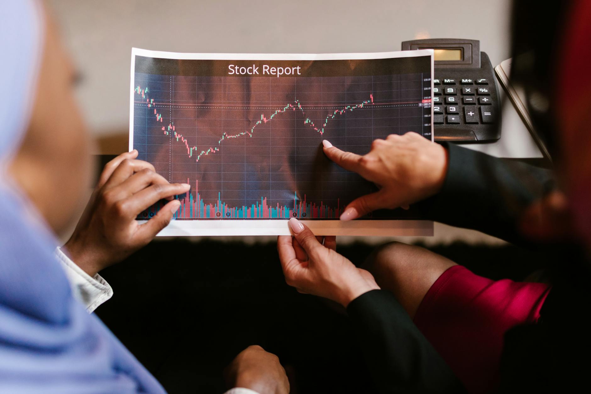 Two professionals discuss a stock report chart in a business meeting, analyzing data trends.