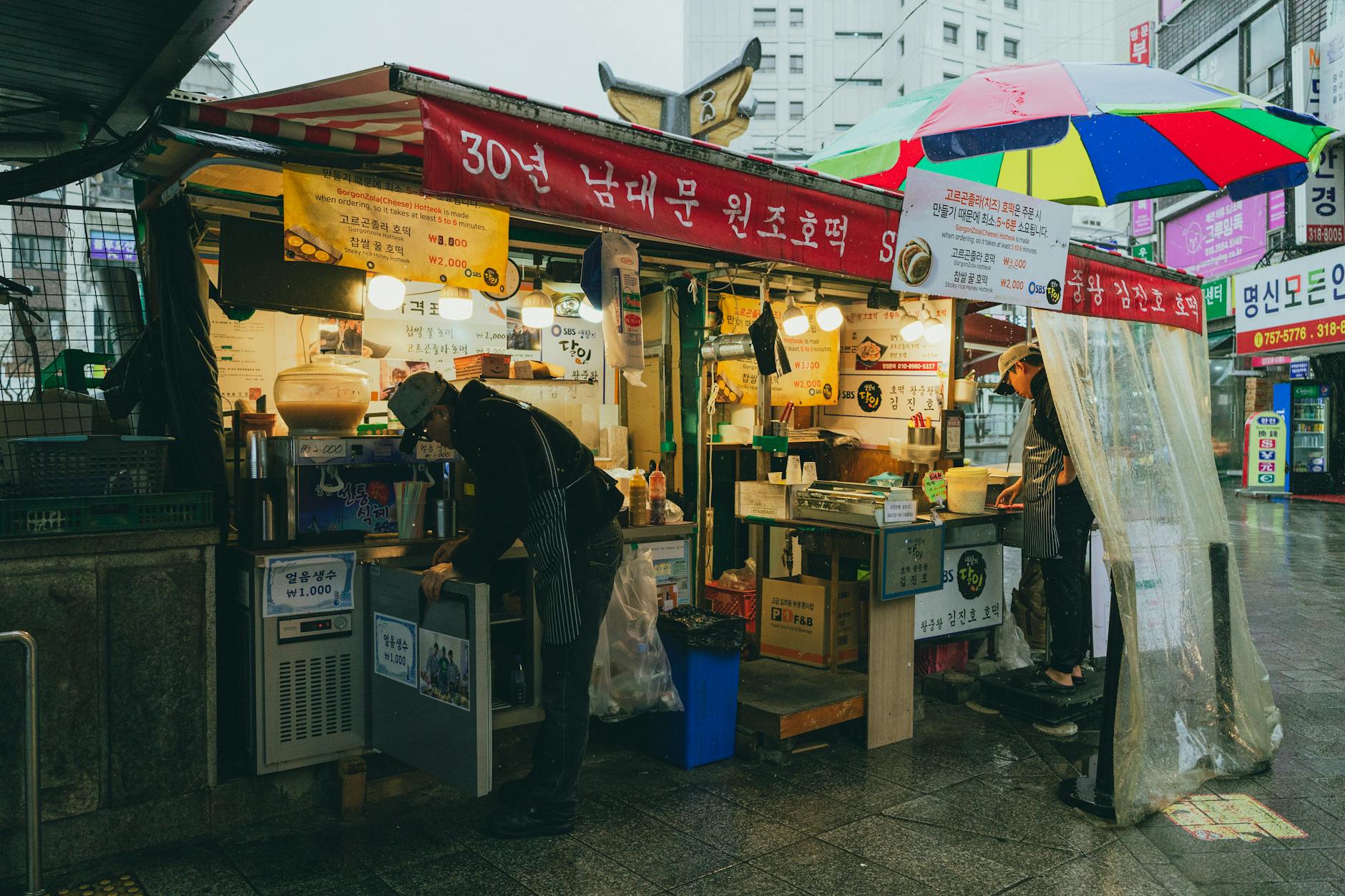 A vibrant street food stall in Seoul's rainy marketplace showcasing Korean culture and cuisine.
