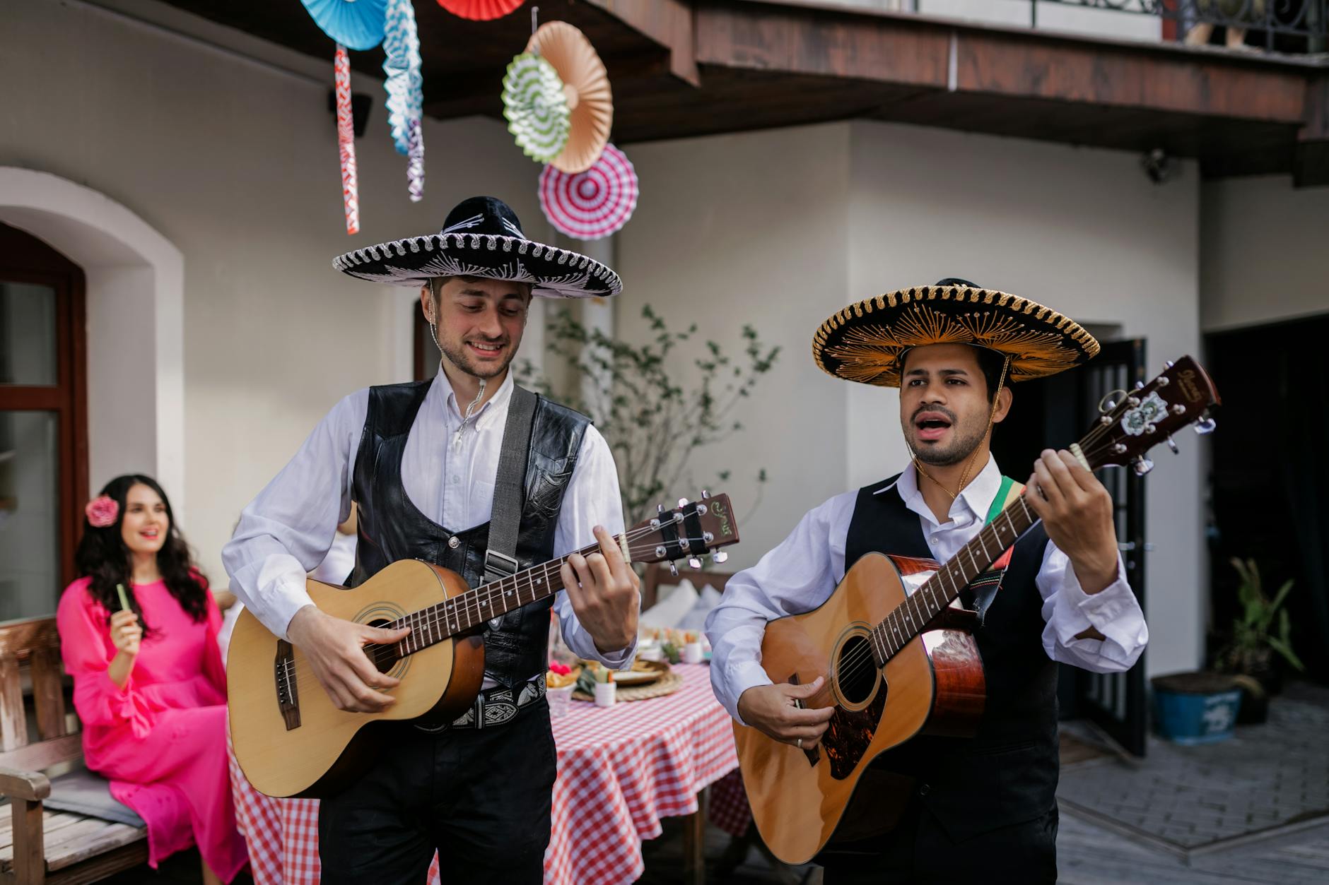 Mexican musicians in sombreros playing guitars at a lively outdoor celebration.