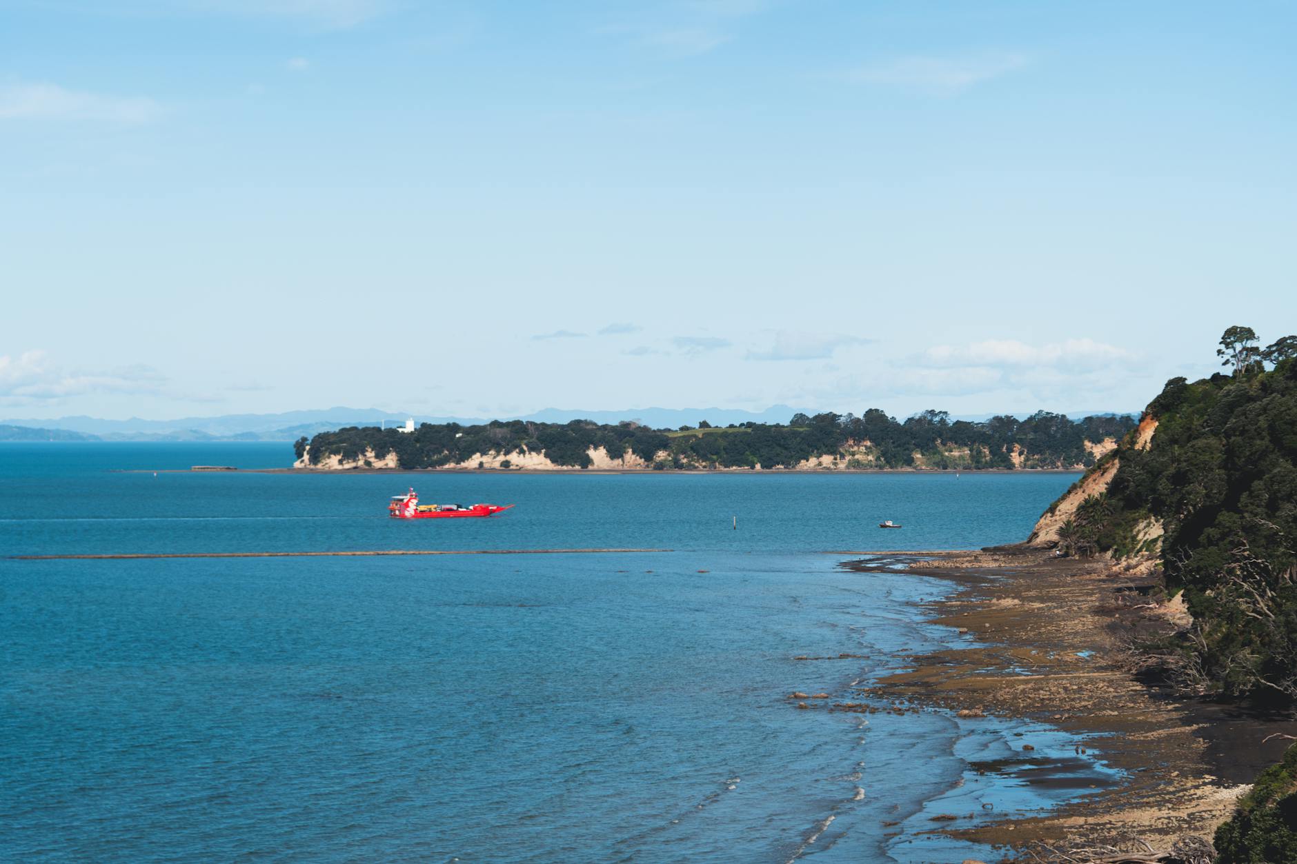 Beautiful coastal view of Rangitoto Island, Auckland with a red boat on the blue ocean.