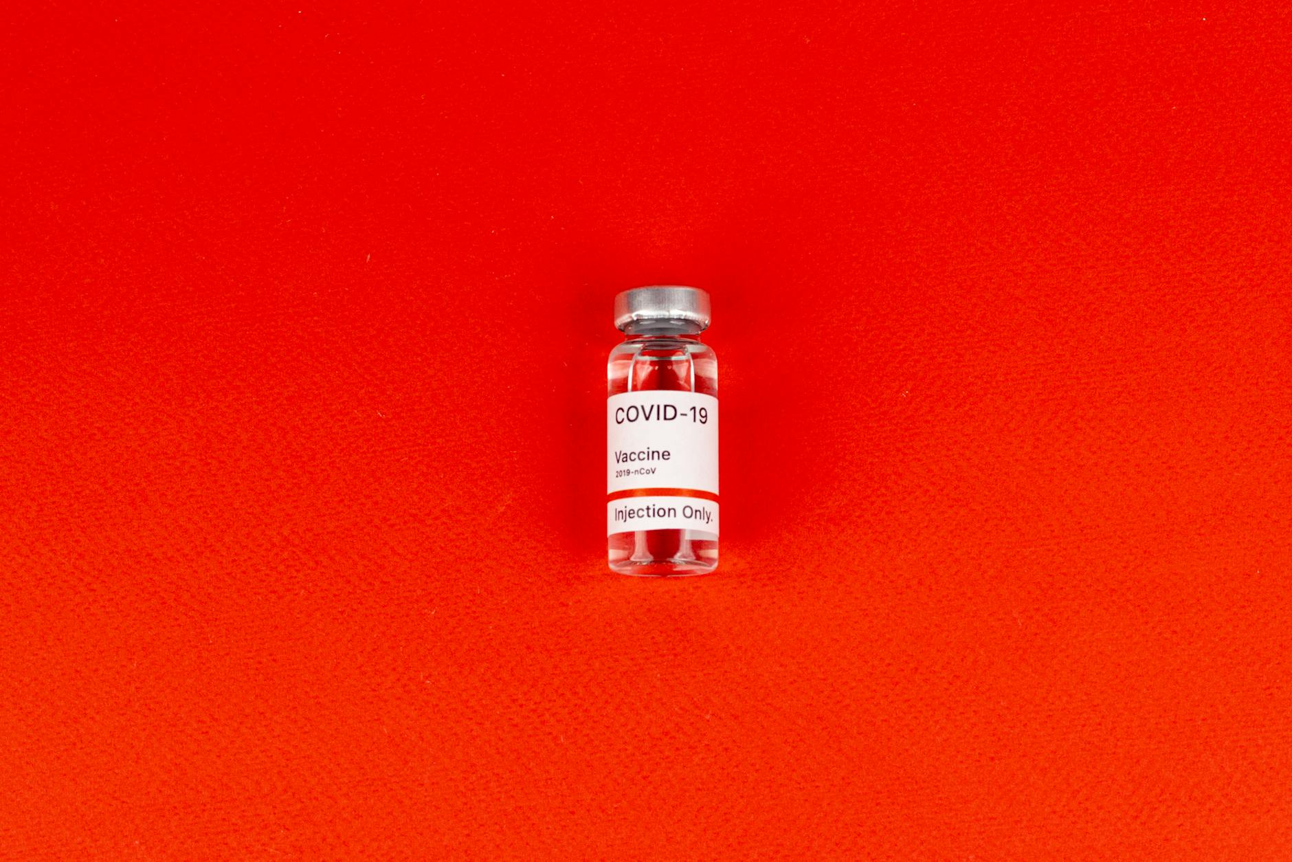 Single COVID-19 vaccine vial on a striking red backdrop, symbolizing health and pandemic response.