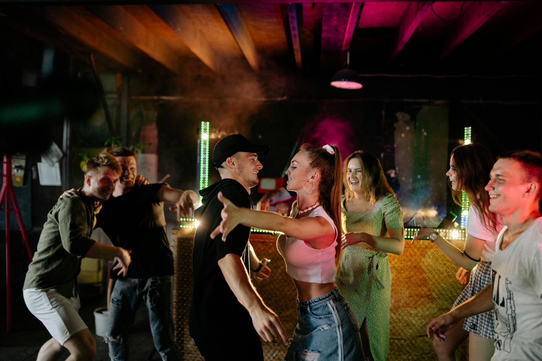 A lively group of young adults dancing at an indoor party. Vibrant lights and energetic atmosphere.