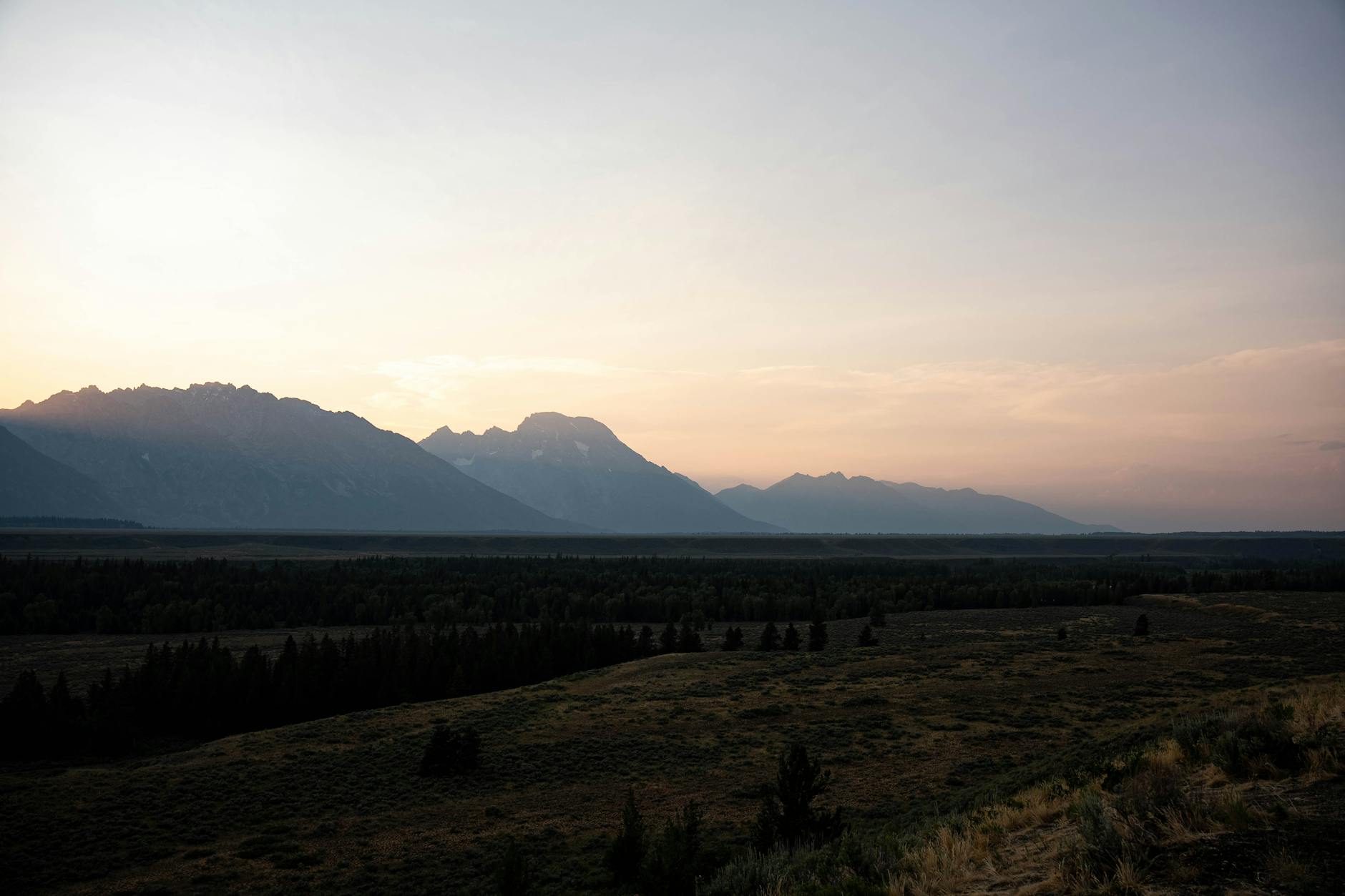 Stunning view of Grand Teton mountains at sunset, featuring silhouettes and expansive landscape.