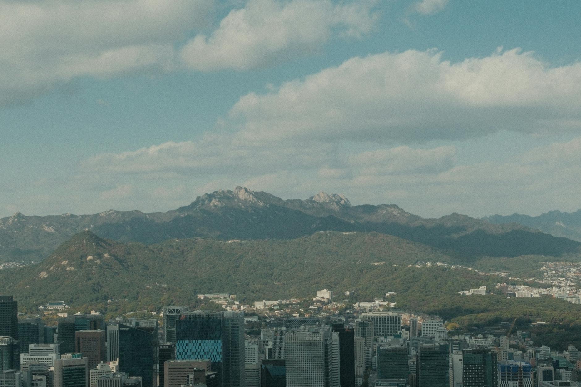 Panoramic view of Seoul's skyline with mountains and a majestic sky in the background.