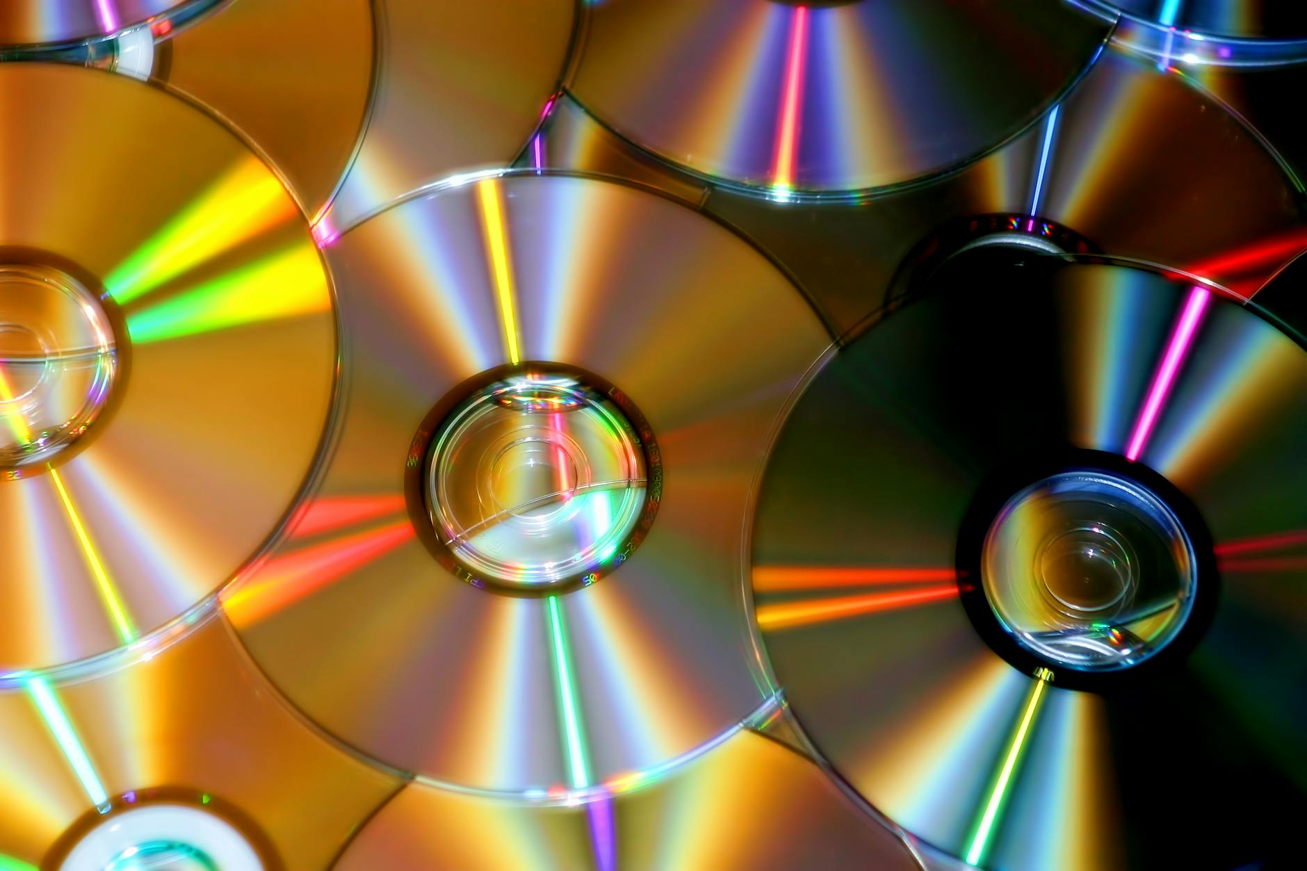 A close-up photo of compact discs reflecting colorful light patterns.