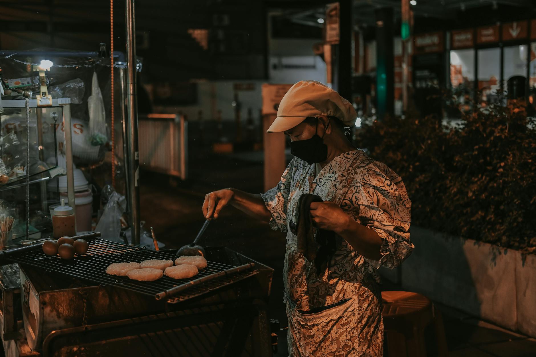 Vendor grilling street food at a lively night market in Bangkok, Thailand.