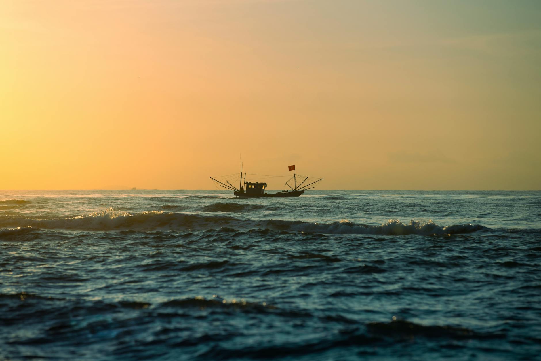A fishing boat sails on the ocean under a vibrant sunrise, creating a serene and captivating scene.