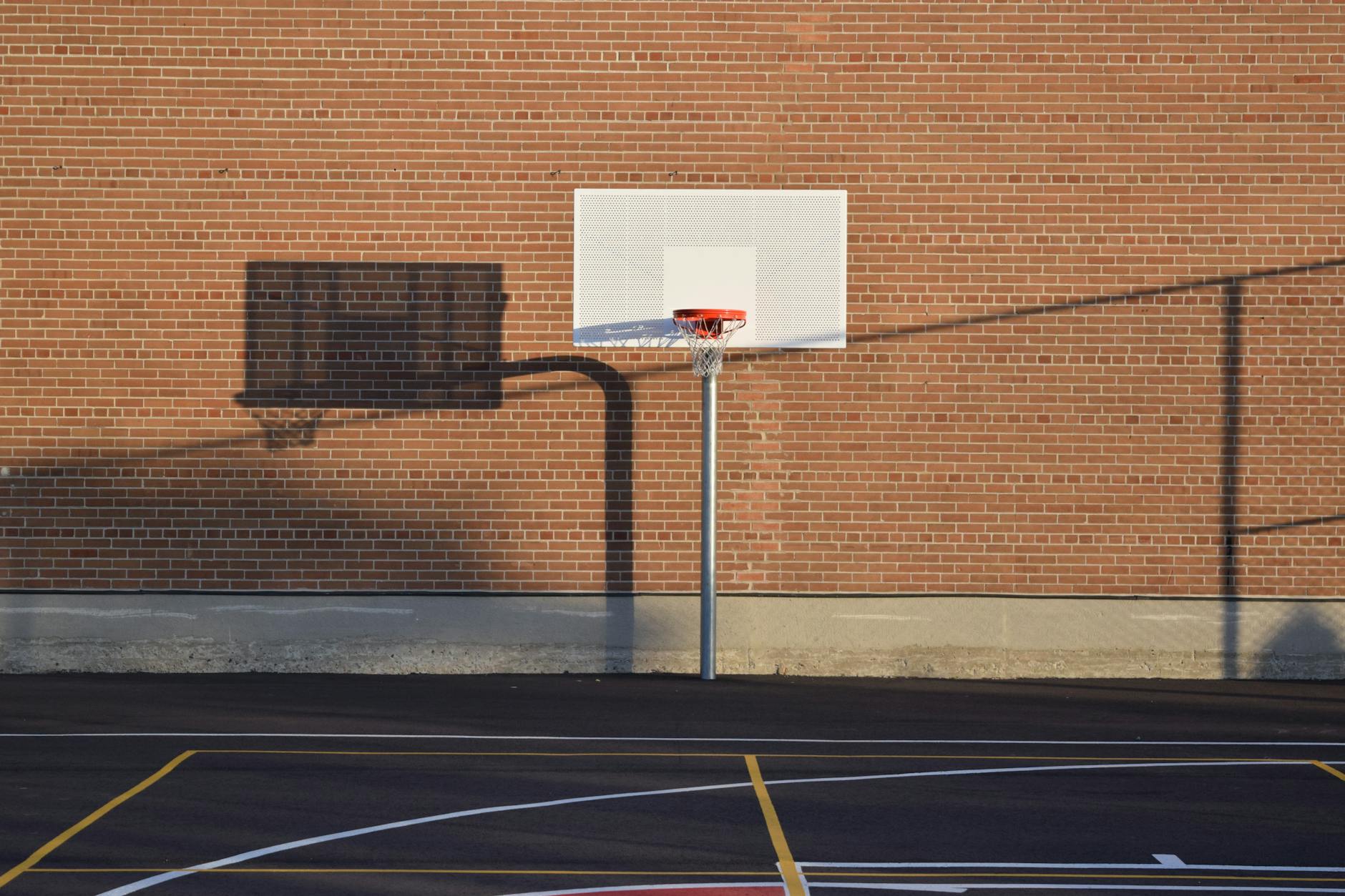 Empty outdoor basketball court with hoop and shadow against brick wall