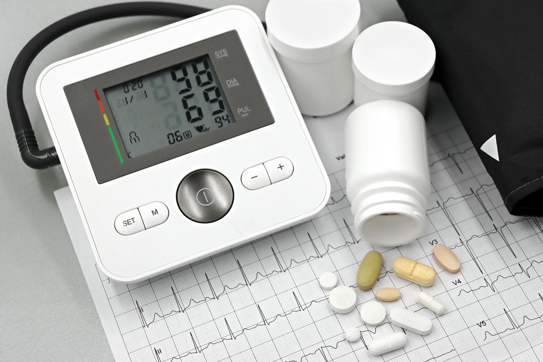 Blood pressure monitor with pills on ECG sheet, essential for heart health management.