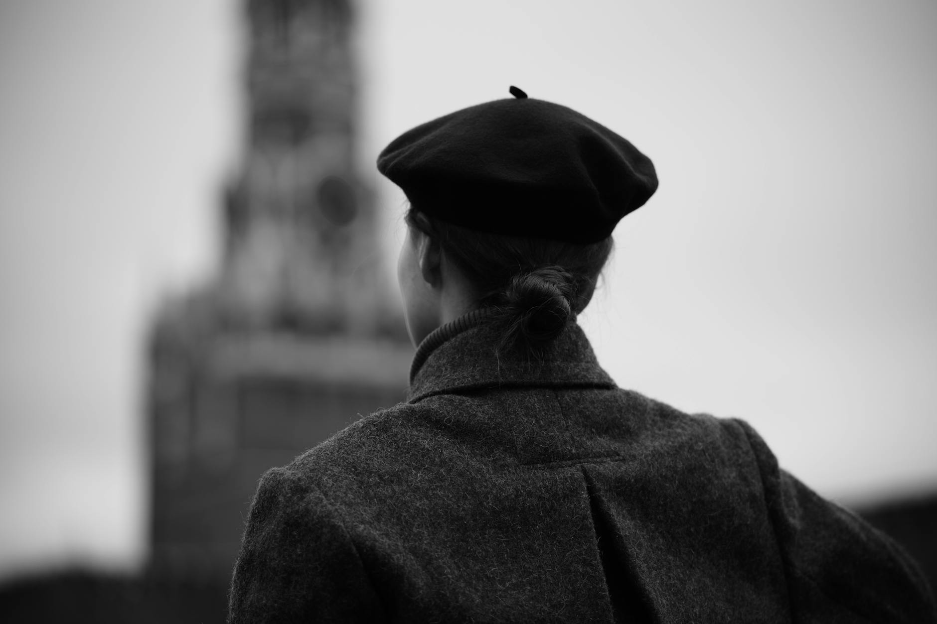 A woman in a beret gazes towards an iconic tower, captured in moody black and white.