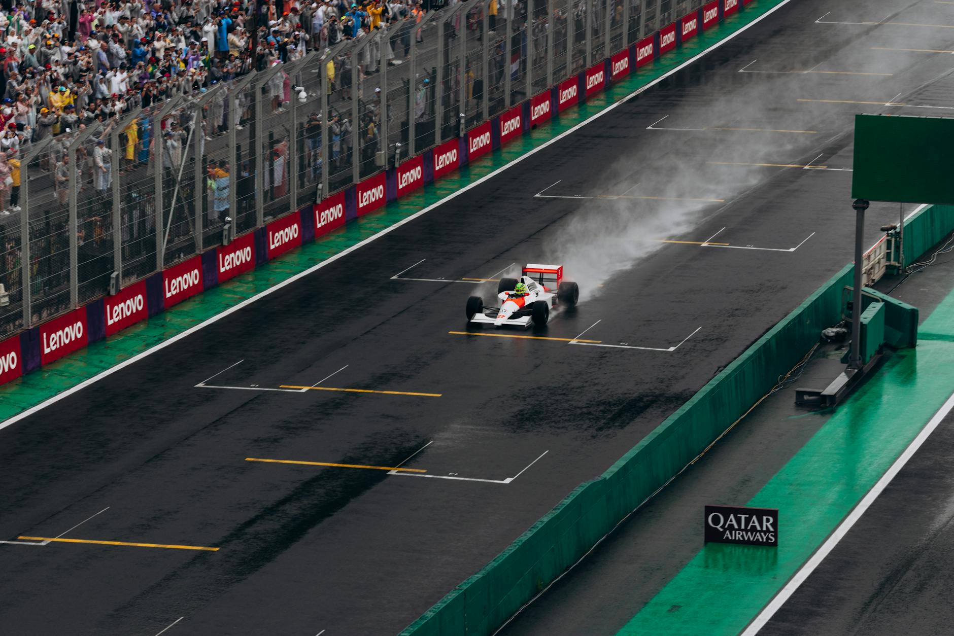 A Formula 1 car speeds through the rain at Interlagos with a cheering crowd.