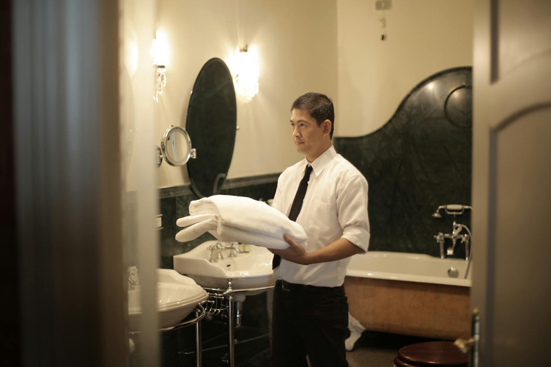 A professional housekeeper arranges towels in a luxury hotel bathroom, emphasizing cleanliness and service.