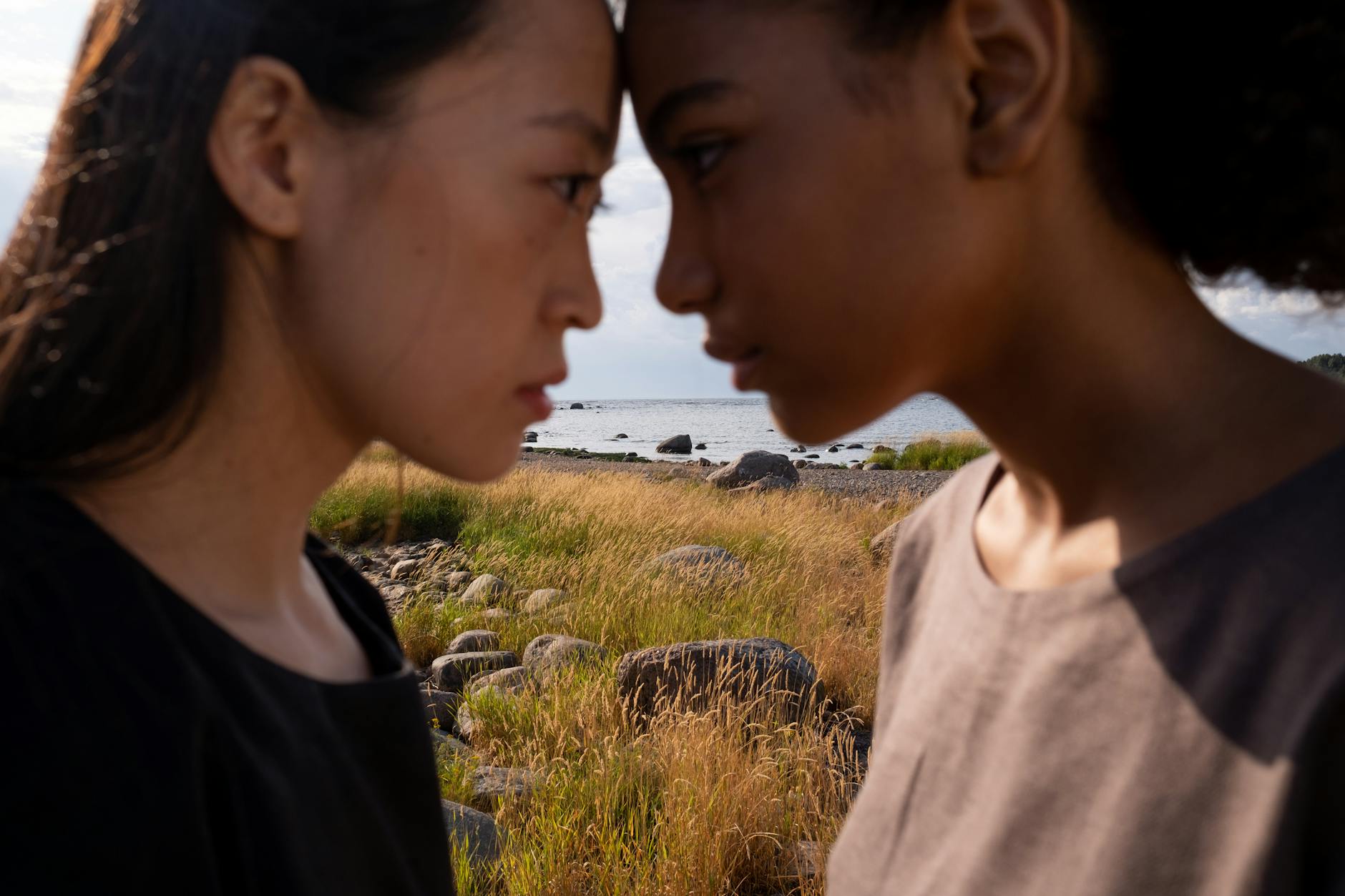 Two women facing each other in a serene outdoor setting by the sea, emphasizing connection.