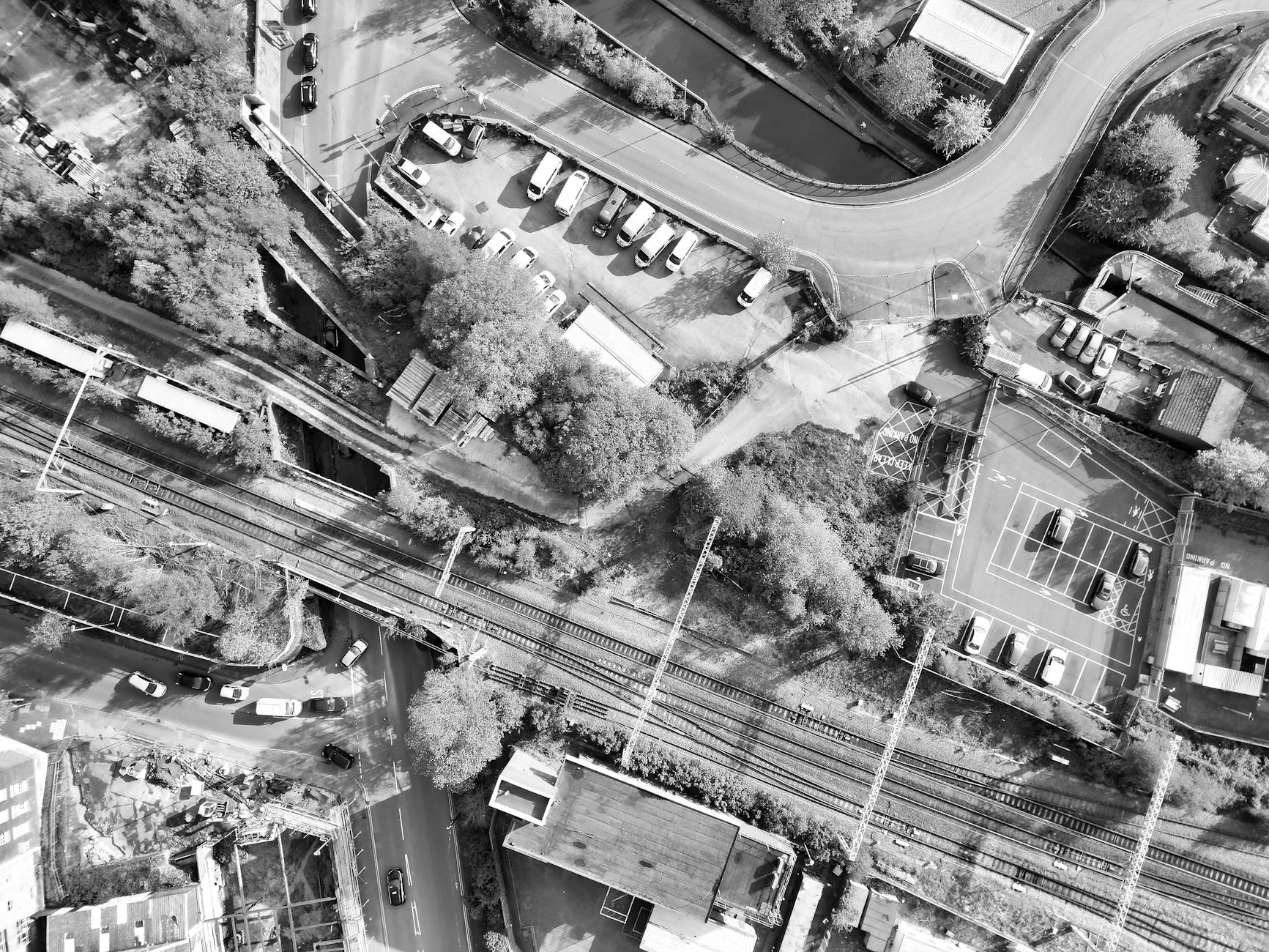 Black and white aerial photograph showcasing urban roads, railways, and parking lots in a suburban setting.