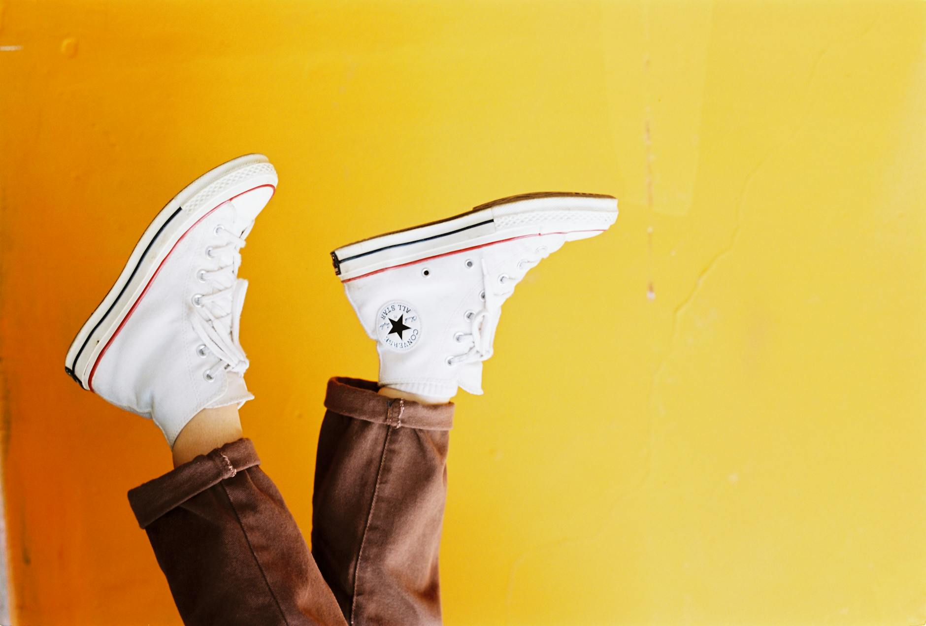Upside down image of white sneakers against a vibrant yellow background, showcasing trendy footwear style.