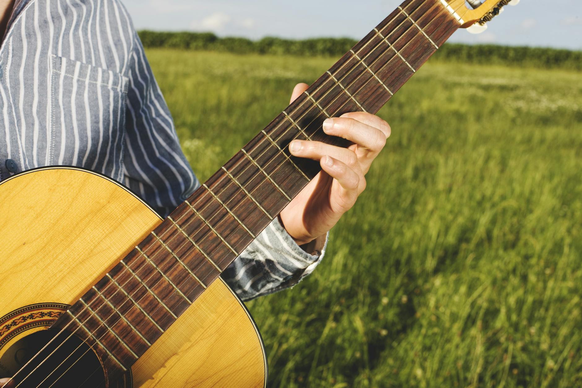 Close-up of a man playing an acoustic guitar outdoors in a sunny field.