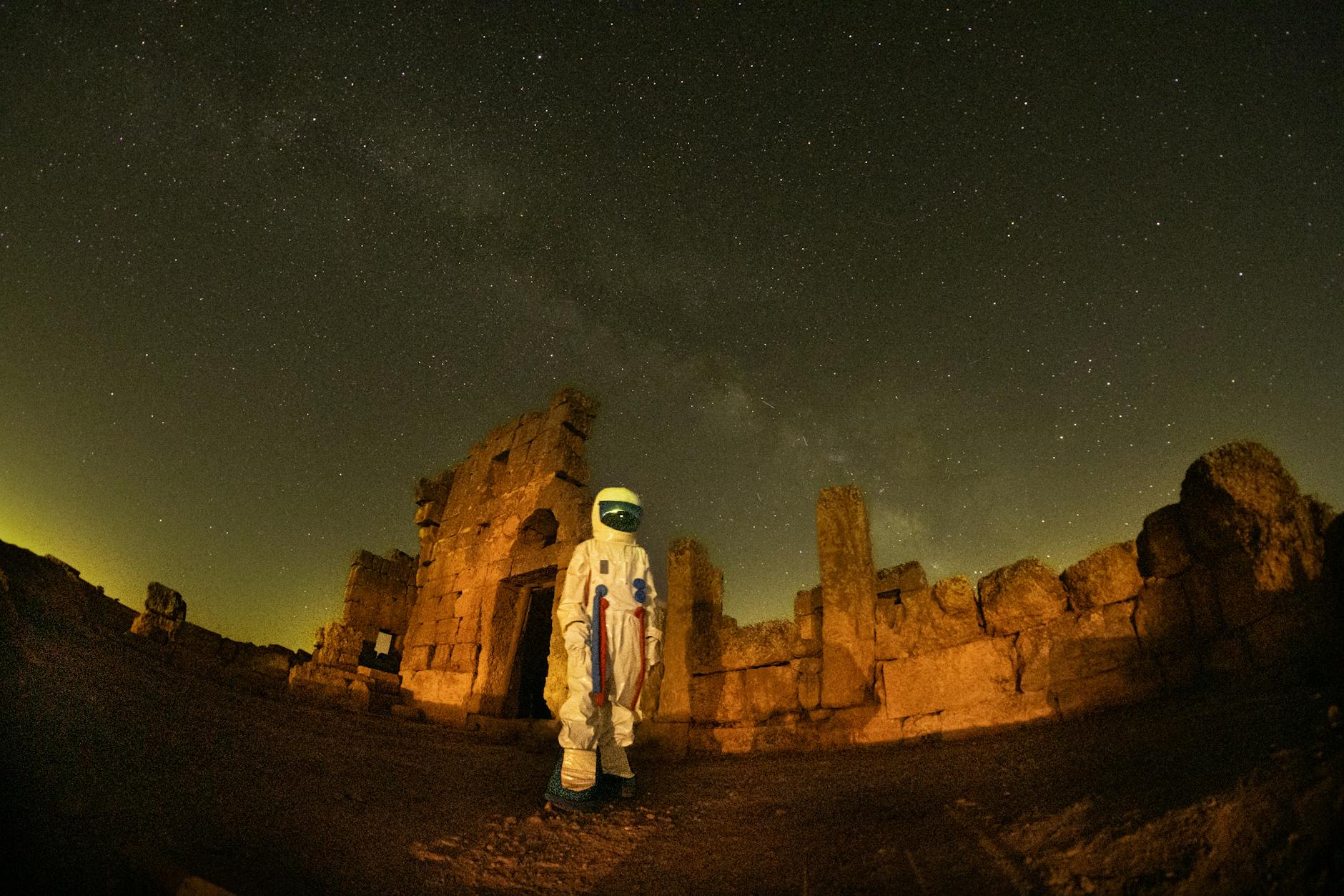 A spacesuit-clad figure stands against the backdrop of ancient Diyarbakır ruins under a starry night sky.