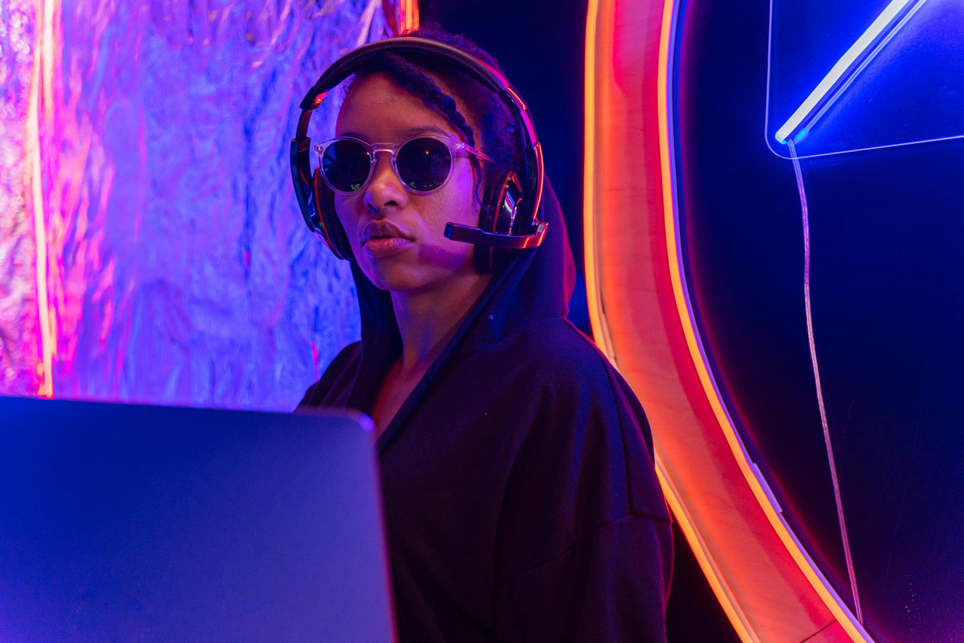 A focused professional in sunglasses and headset monitors cybersecurity in a neon-lit room.