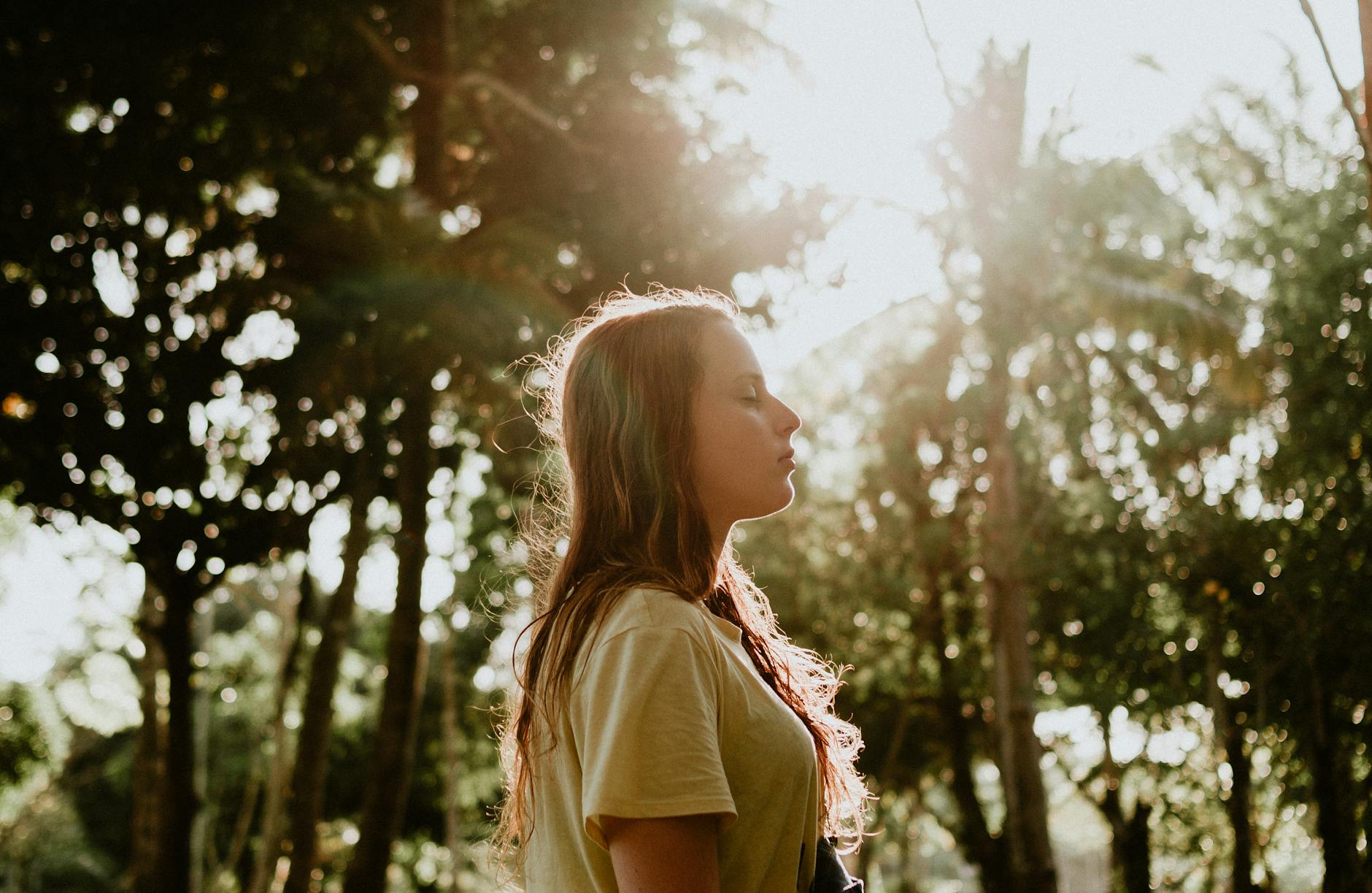 Young woman with closed eyes enjoying a peaceful moment outdoors in sunlight.