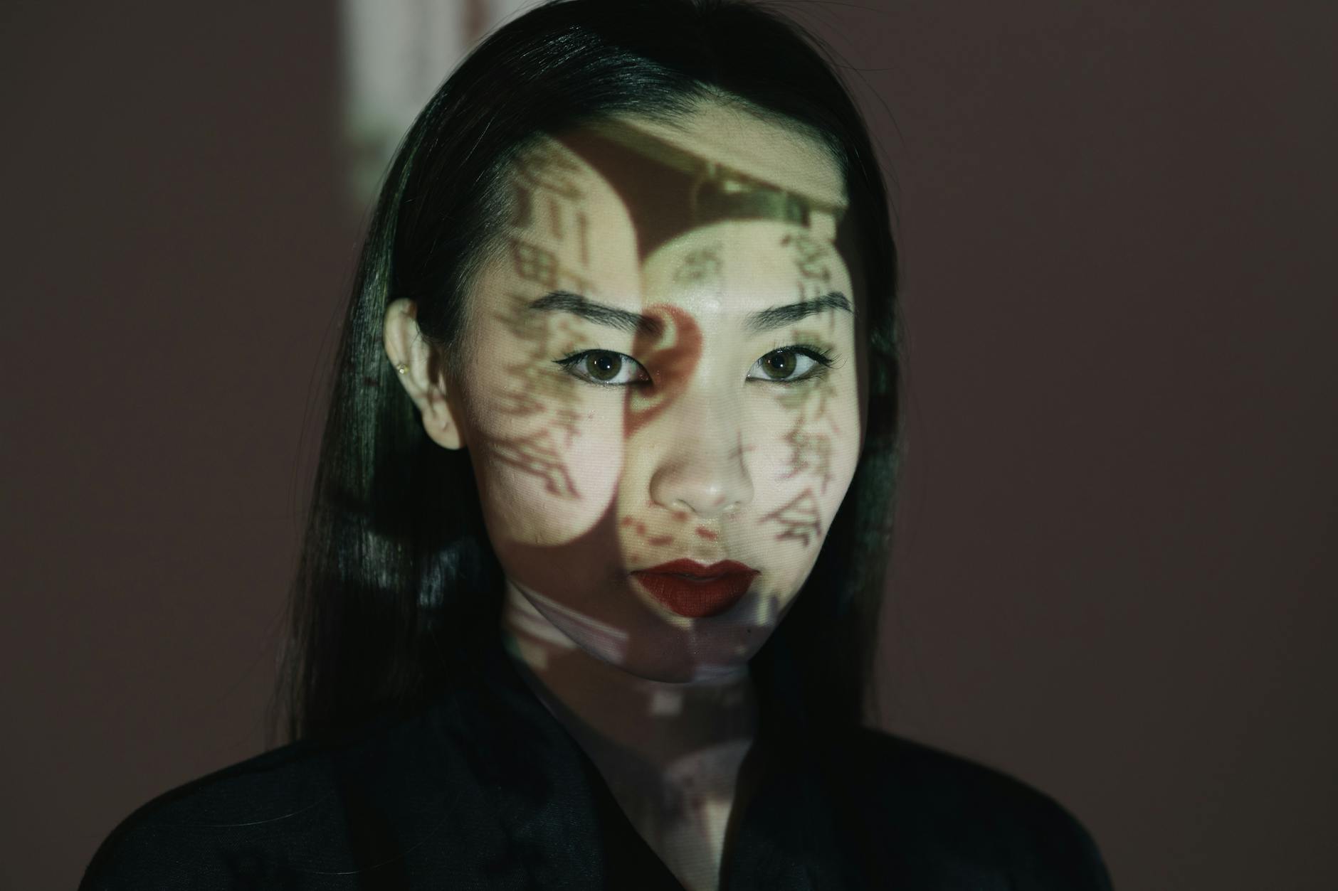 Creative portrait of an Asian woman with projected text and dramatic shadows.