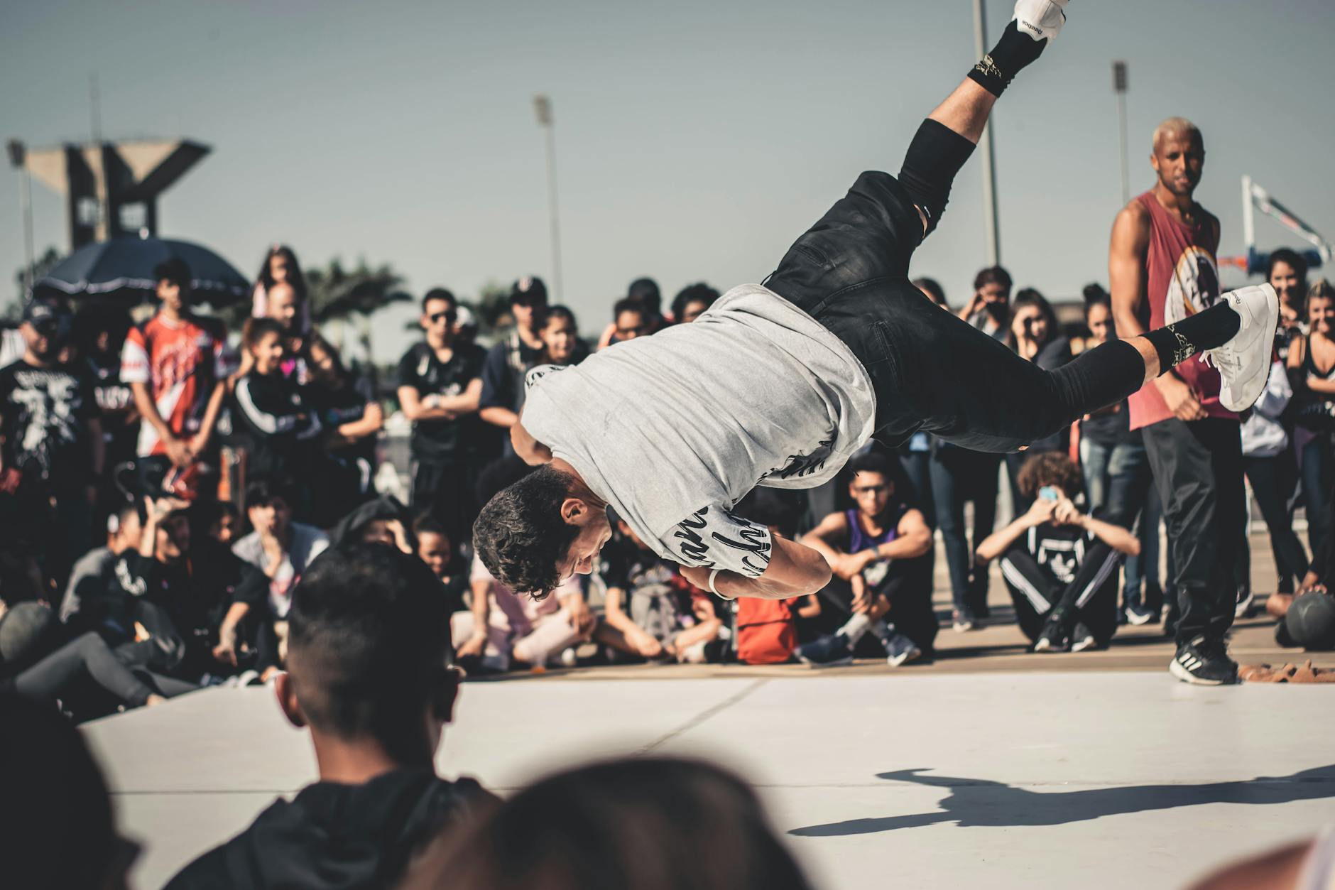 Energetic breakdancer performing a flip in front of an engaged audience during a sunny street festival.