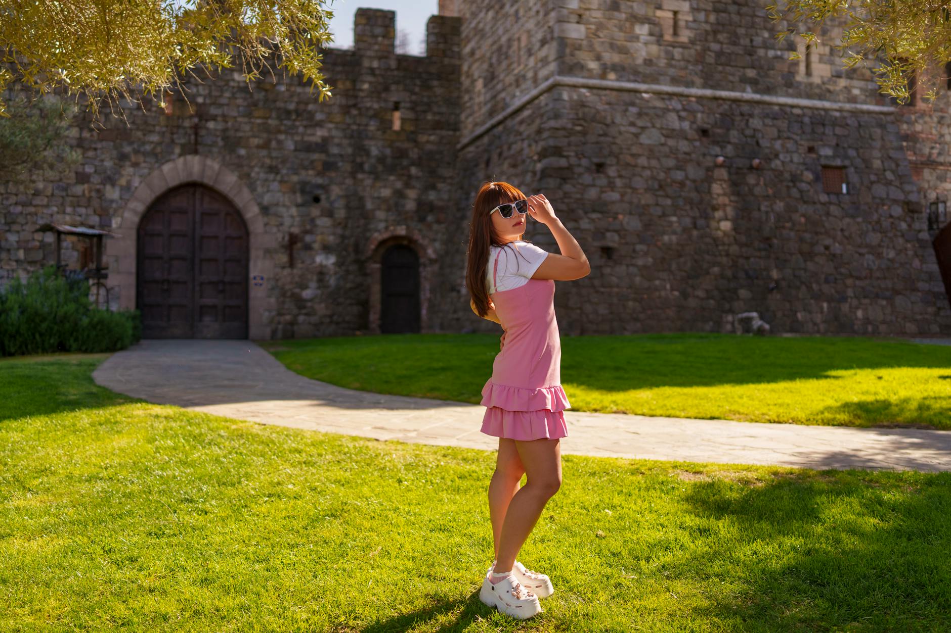 Woman in sunglasses and pink dress poses by historic stone castle in Calistoga, California.