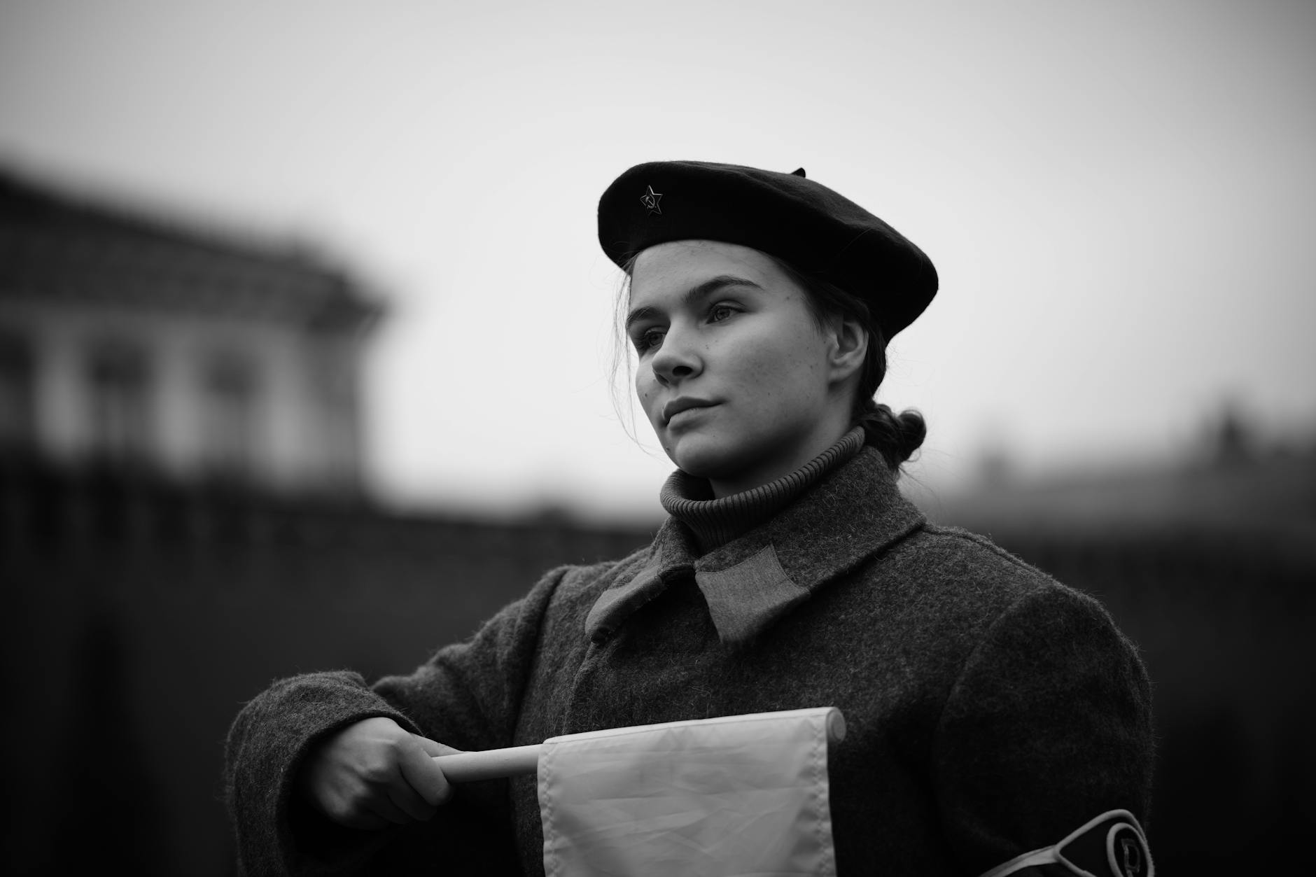Black and white portrait of a woman in vintage military attire holding a flag.
