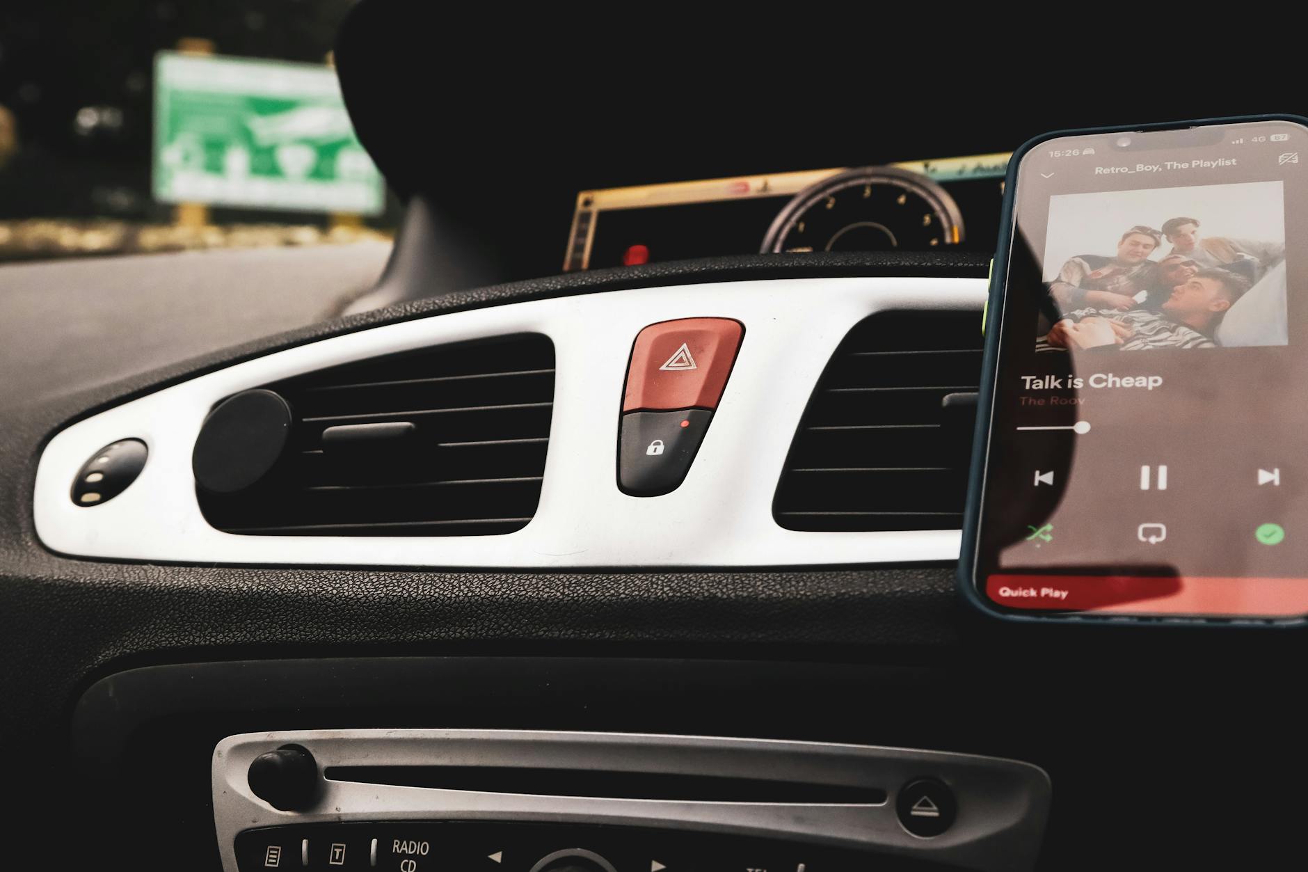 Car interior with smartphone on Spotify and dashboard controls in focus.