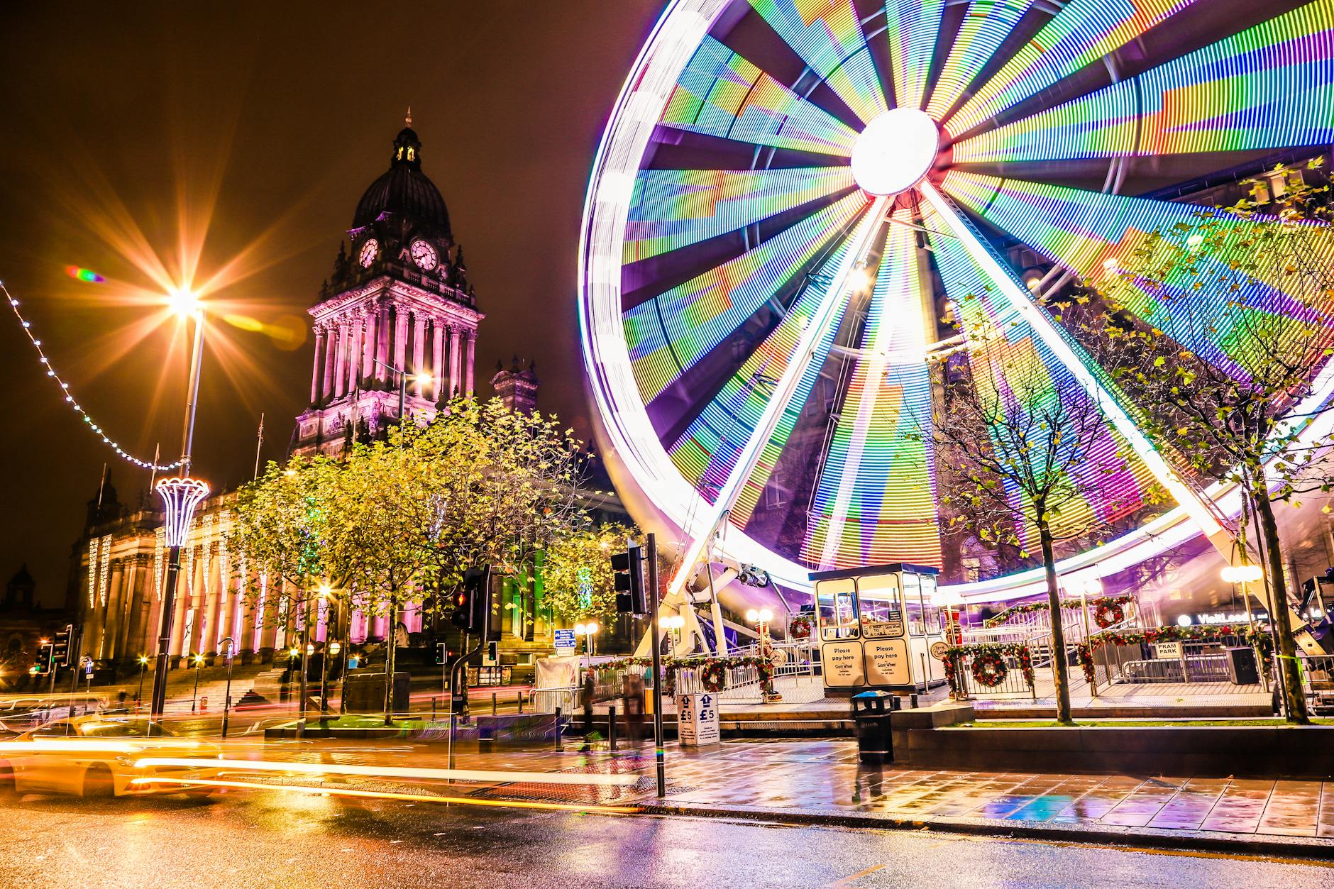 Vibrant night scene featuring Leeds Town Hall and illuminated Ferris Wheel, showcasing colorful city life.