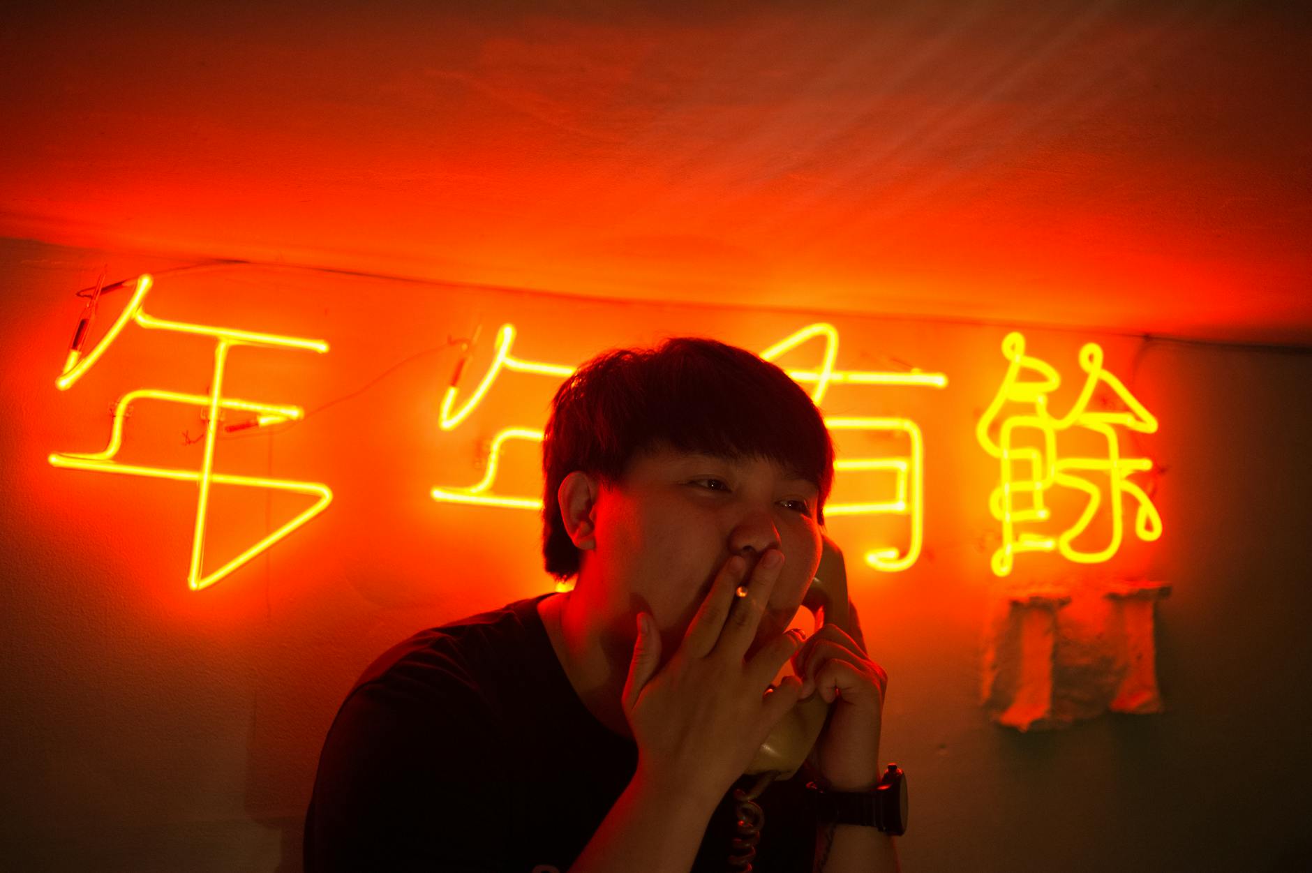 A person smokes inside a room illuminated by bright neon orange signs, creating a moody atmosphere.