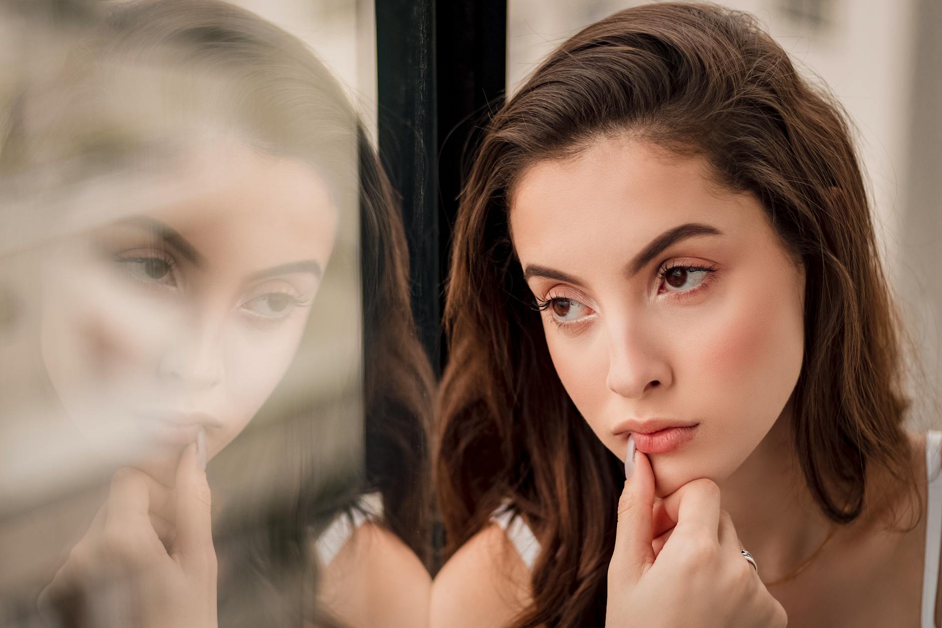 A pensive woman looks out a window, her reflection creating a thoughtful portrait.
