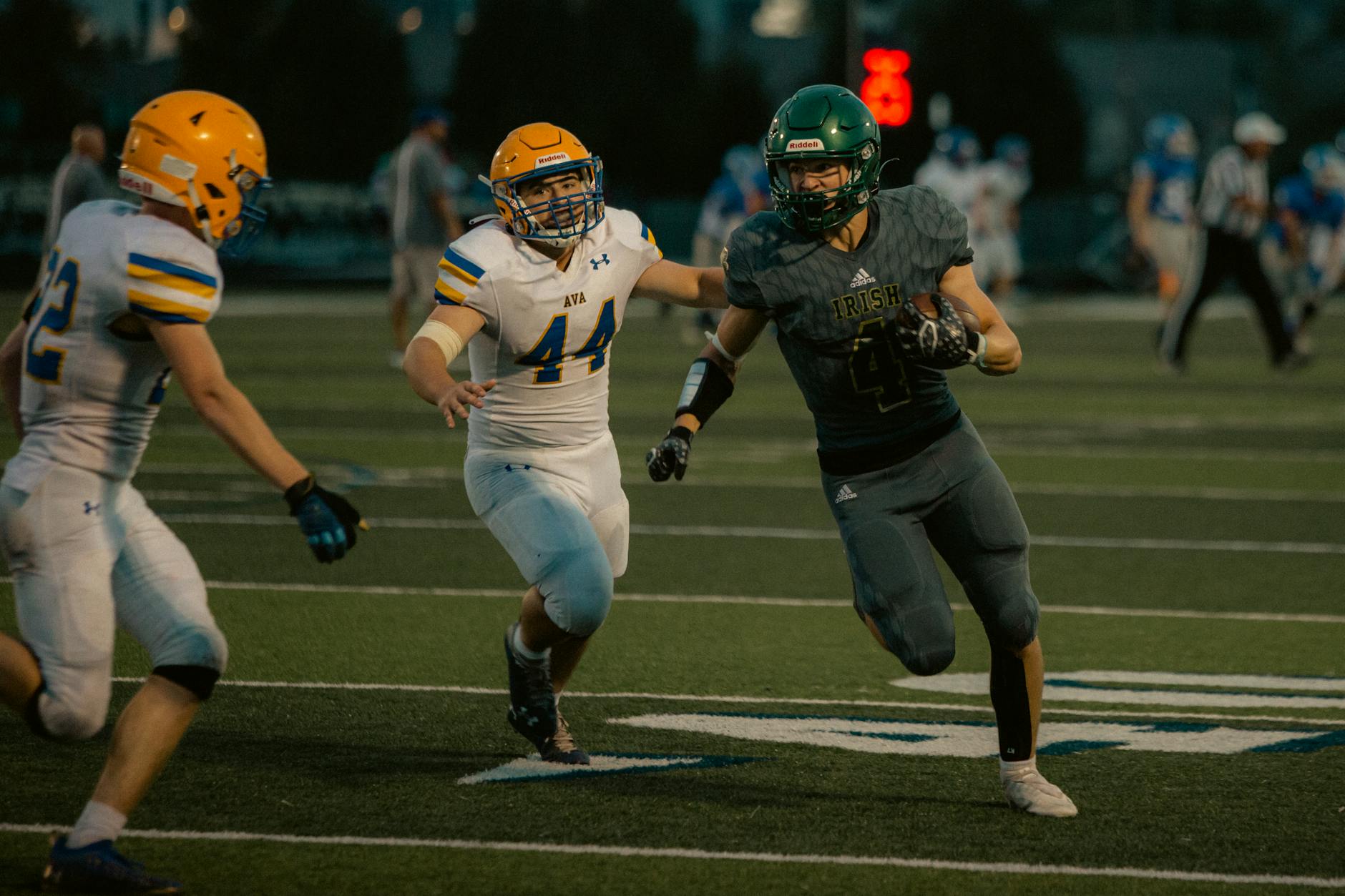 High school football players in action during an evening game under stadium lights.