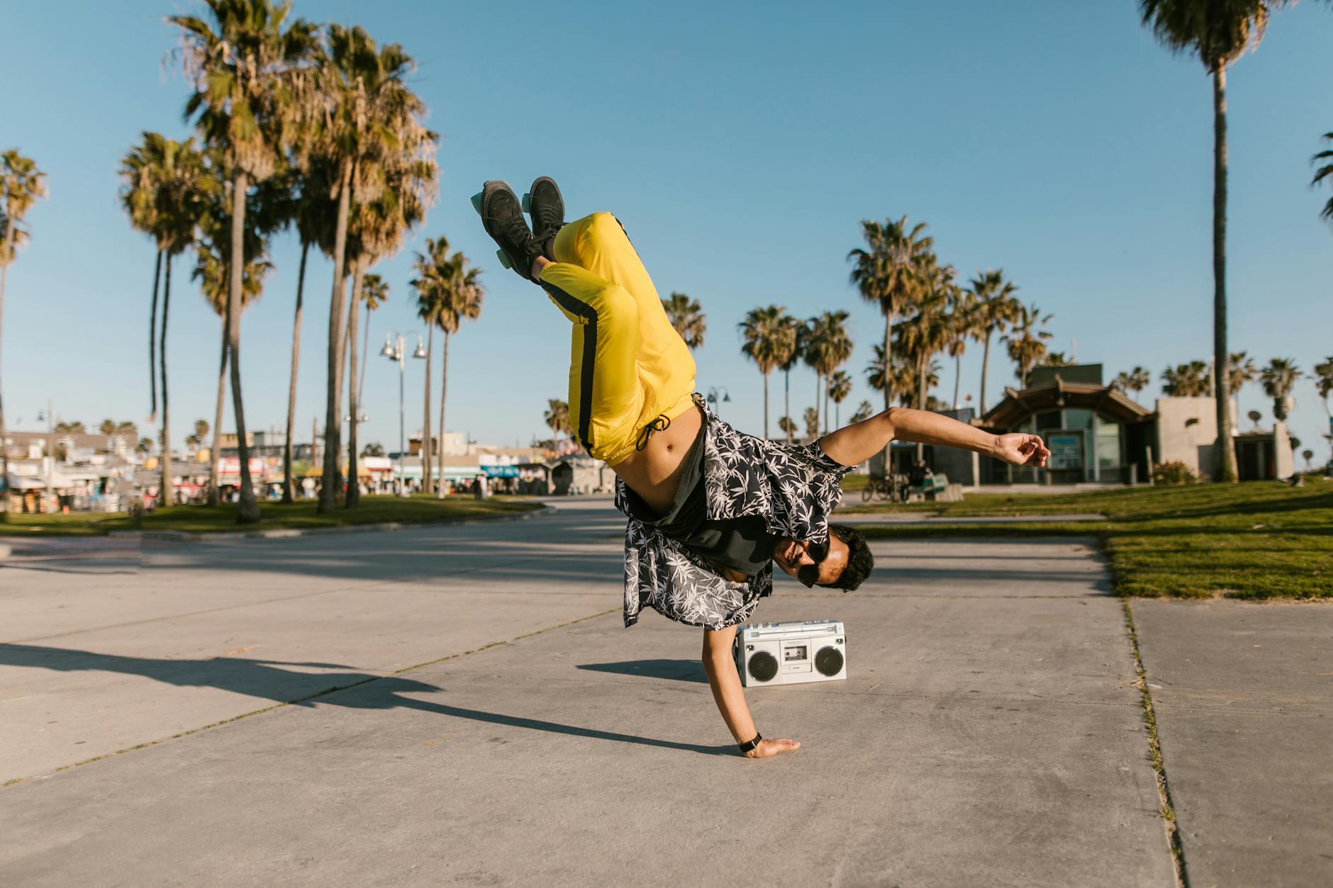 Young skater performing a hand stand with a boombox in a sunny Californian park.